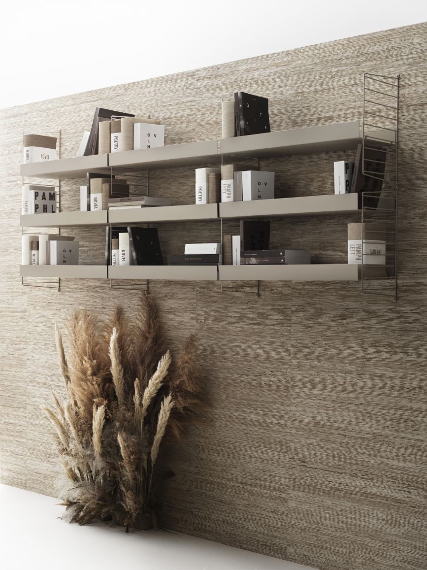 Beige String Furniture Wandregal mit Bücher und Dekoration vor einer strukturierten Wand.