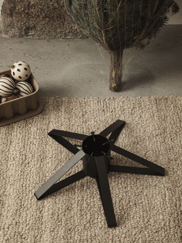 Schwarzer Christbaumständer von Ferm Living auf einem Teppich, bereit für den Weihnachtsbaum.