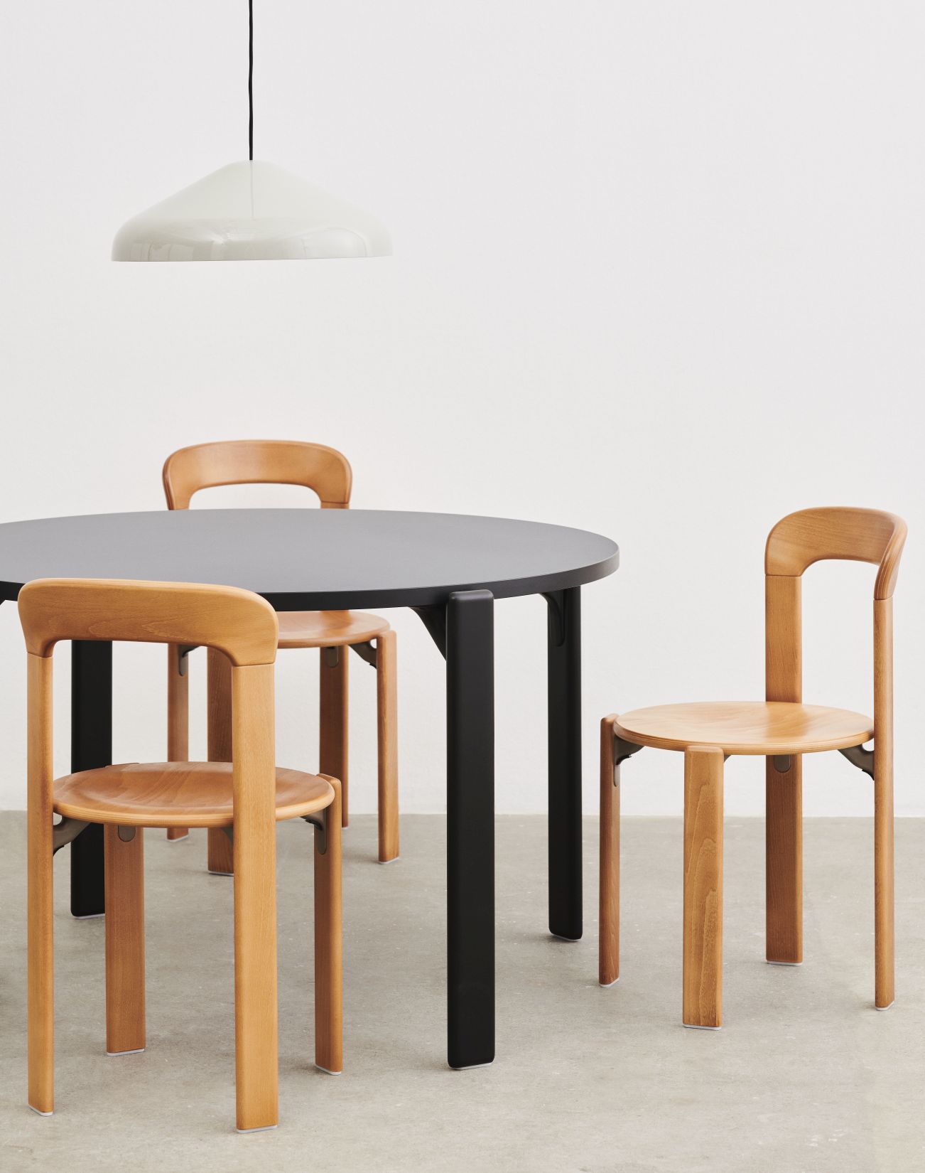 Schwarzer Rey Table Tisch von Hay mit Holzstühlen und Pendelleuchte vor weißem Hintergrund.