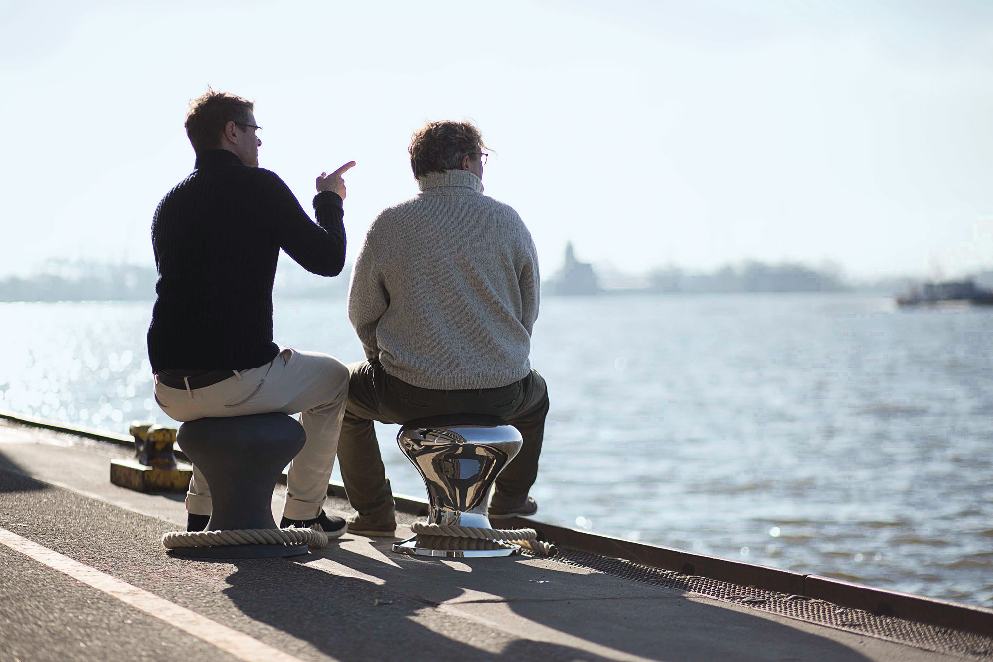 Zwei Männer sitzen auf Philippi Hockern am Wasser. Design Hocker für stilvolles Sitzen.