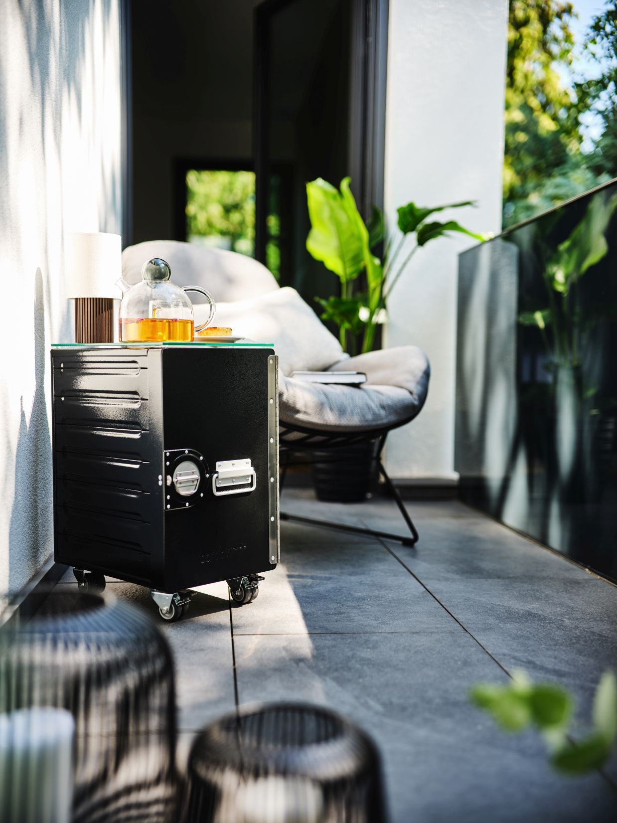 Schwarzer Outdoor-Servierwagen mit Glasplatte und Teekanne auf einer Terrasse, ideal für Garten und Balkon.