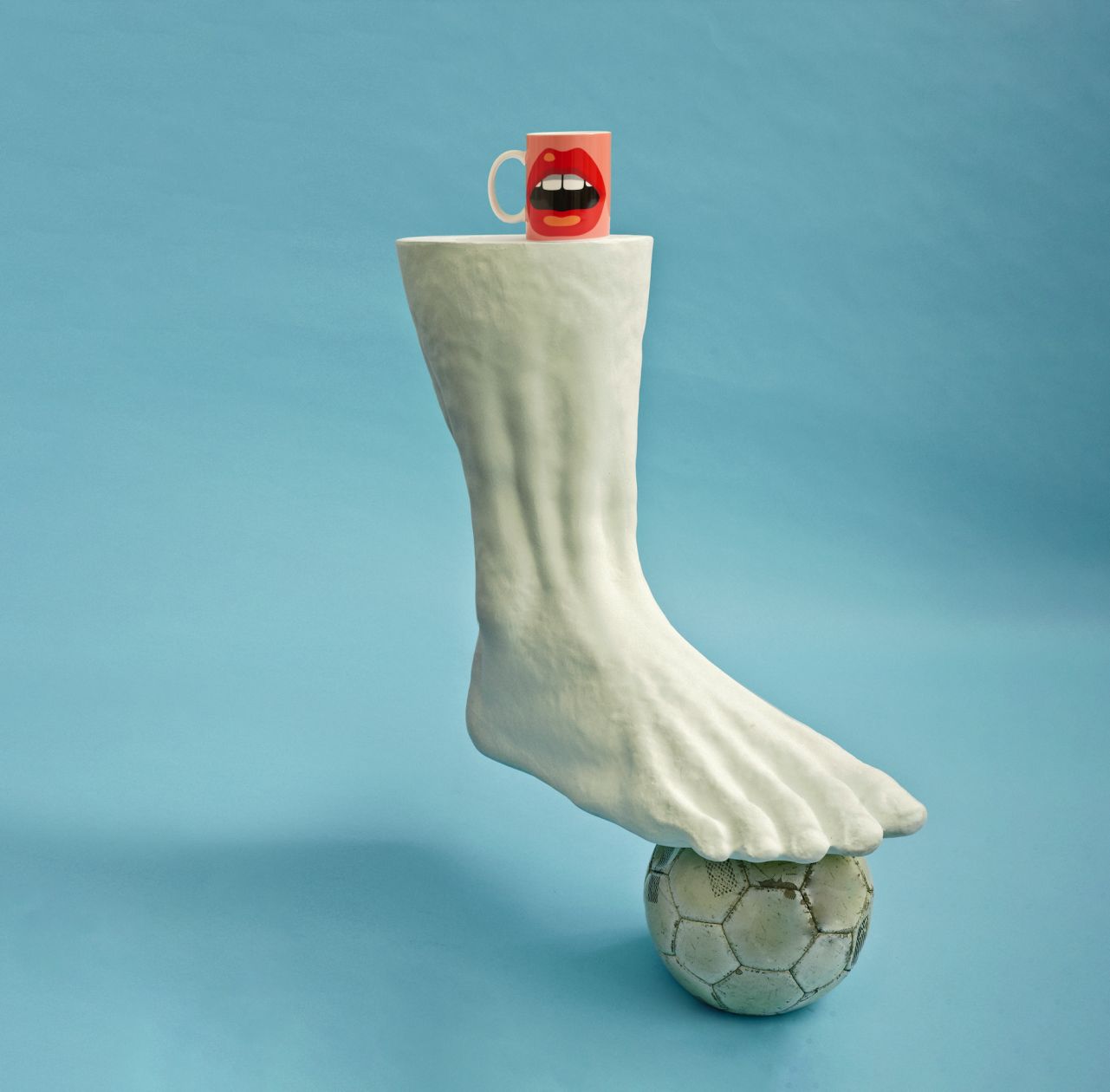 Colossus Beistelltisch von Seletti: Skulpturaler Tischfuß in Fußform, balancierend auf Fußball, mit Tasse.