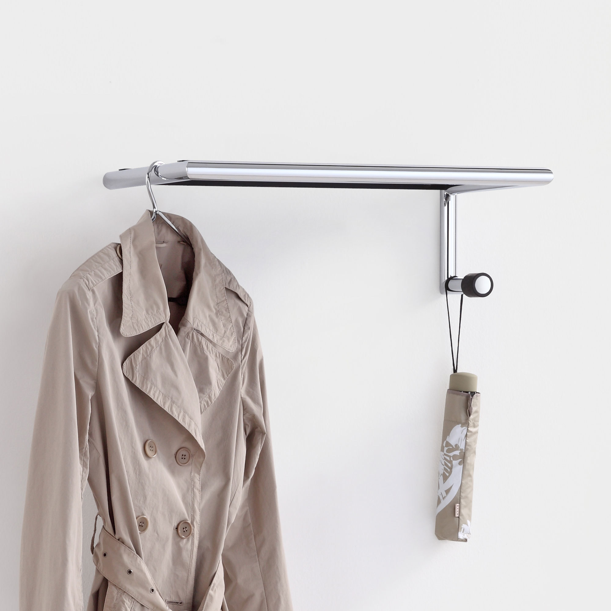 Link 55 Wandgarderobe mit Hutablage: Chromfarbene Garderobe mit Mantel und Regenschirm an weißer Wand.