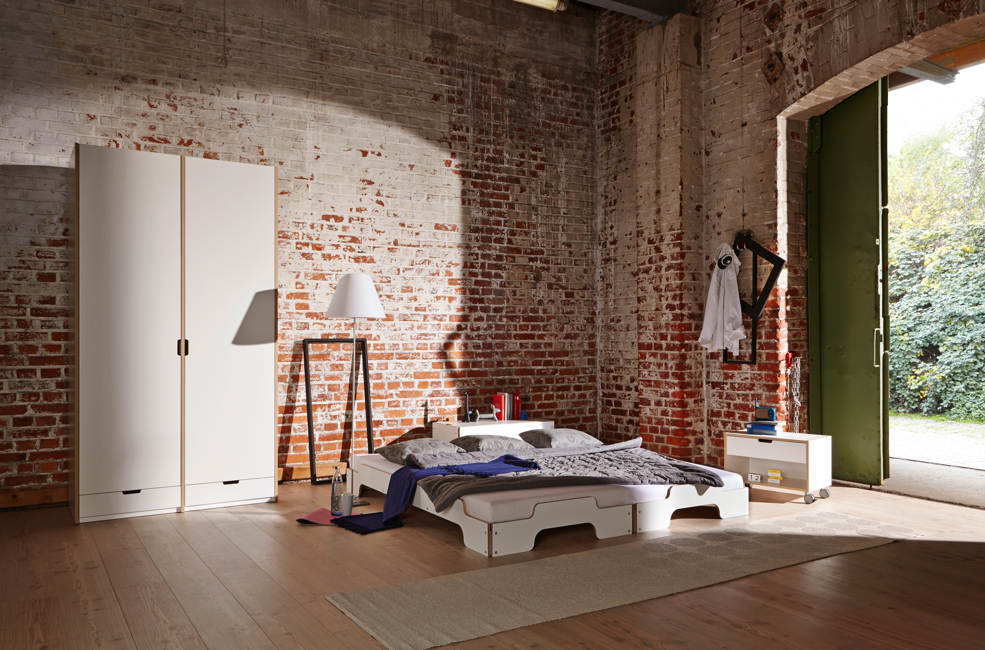 Helles Zimmer mit weißer Stapelliege von Müller Möbelwerkstätten, Kleiderschrank und Ziegelwand. Modernes Bett im Loft.