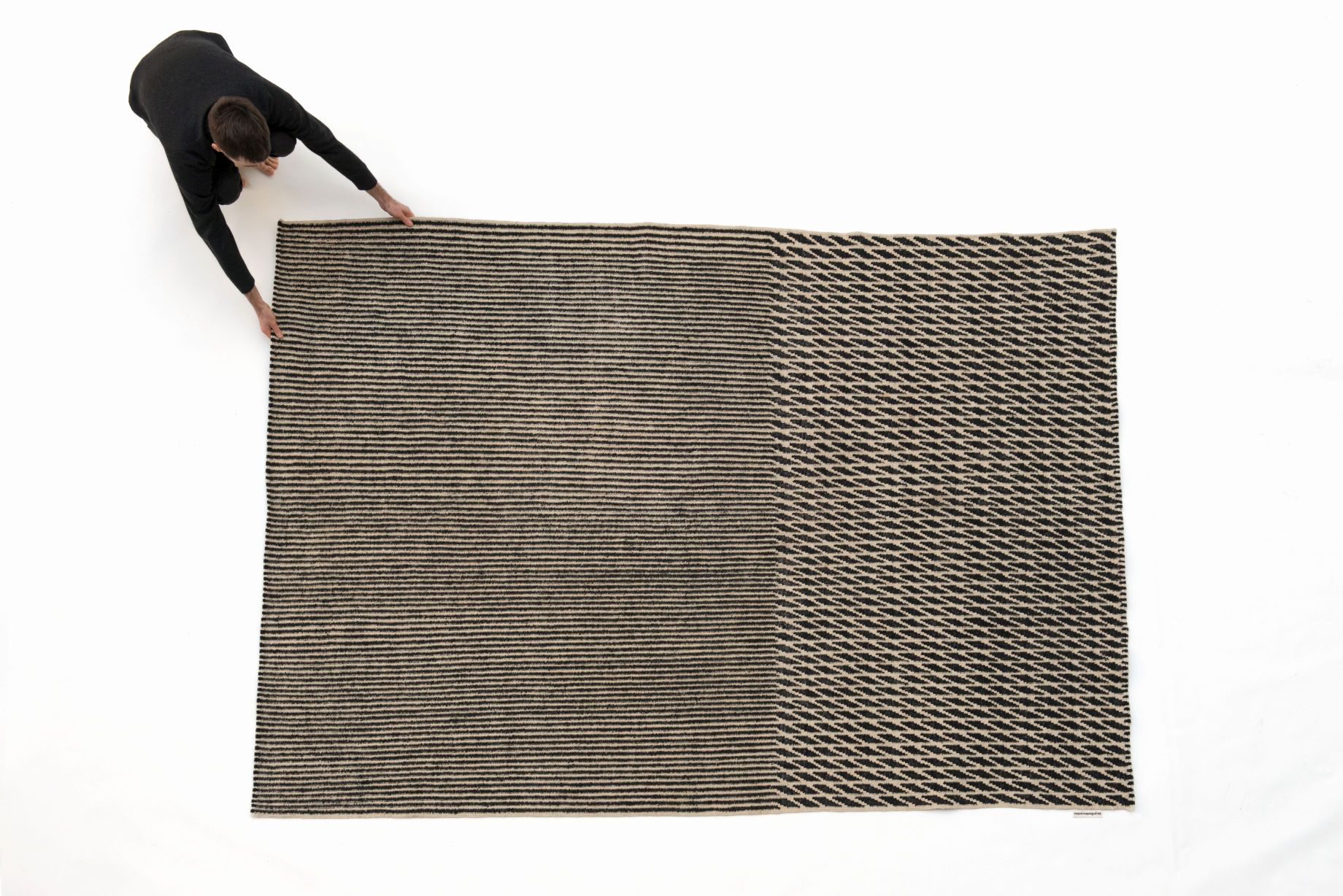 Draufsicht: Person rollt den modernen Nanimarquina Blur Teppich mit abstraktem Muster aus.