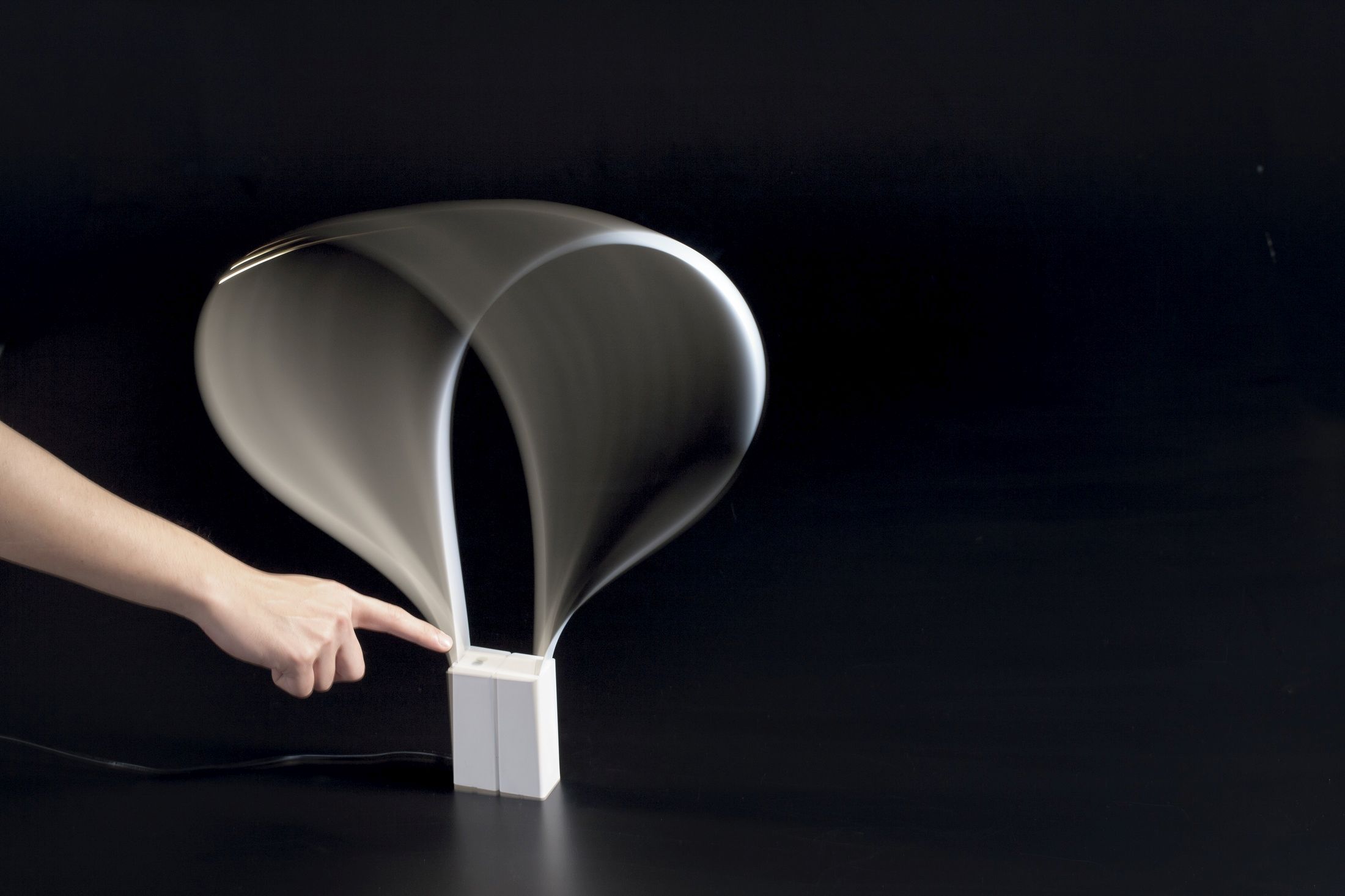 Fluida Tischleuchte von Martinelli Luce: Moderne Designleuchte mit dynamischer Form und Finger am Schalter.