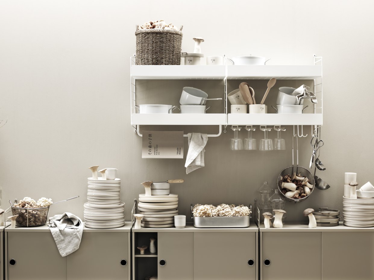 Wohnzimmer mit String Furniture Regalsystem, Geschirr, Kochutensilien und Dekoration in neutralen Farben.