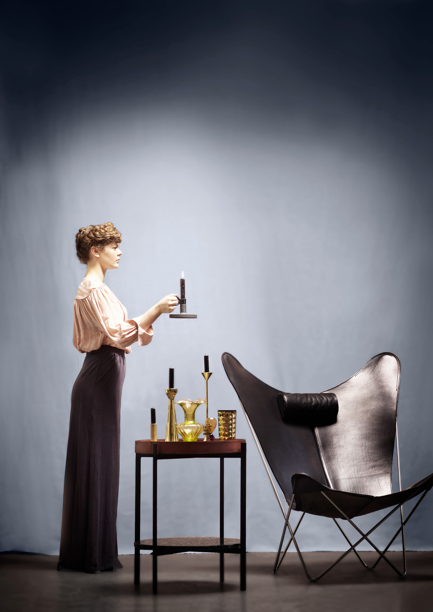 Frau zündet Kerze auf Deck Beistelltisch von Ox Denmarq an, Leder und Holz, neben Sessel.