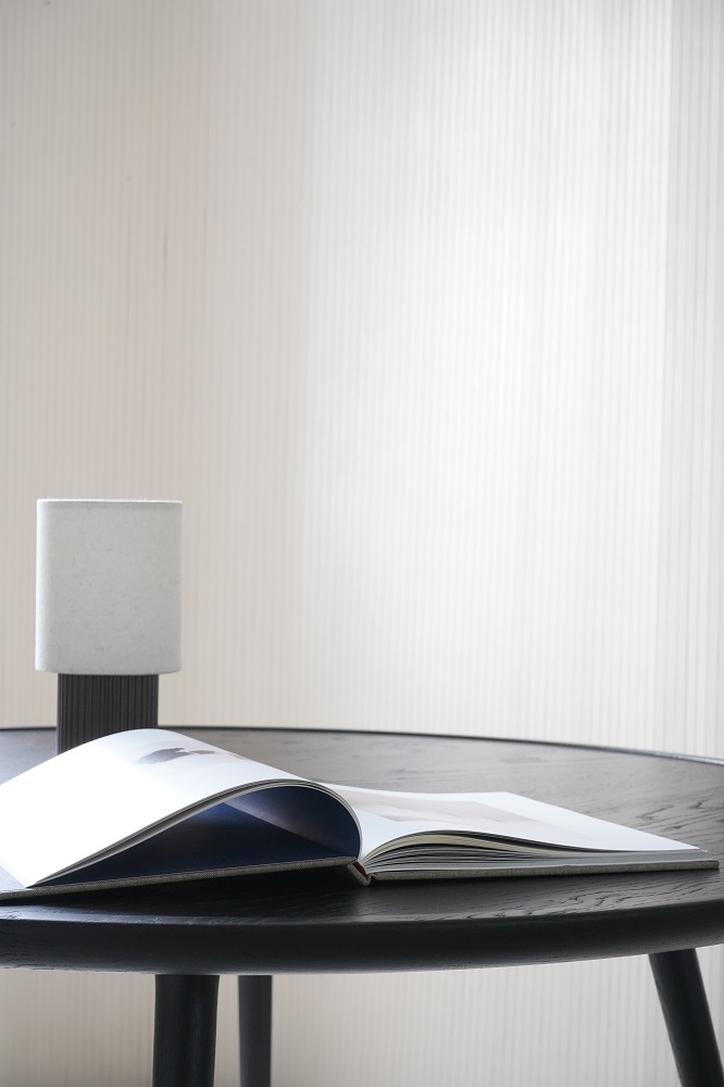 Detailaufnahme: Runder Esstisch aus Eiche, schwarz gebeizt, mit Buch und Lampe. Mater Design.