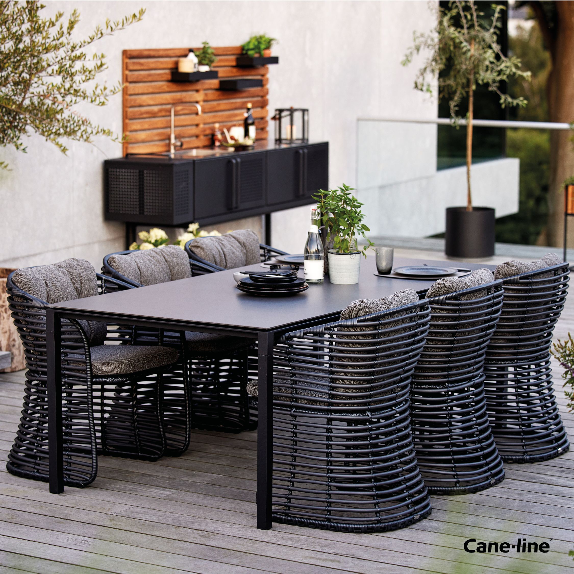 Cane-Line Basket Sessel Graphit mit grauen Kissen und Esstisch für den Garten.