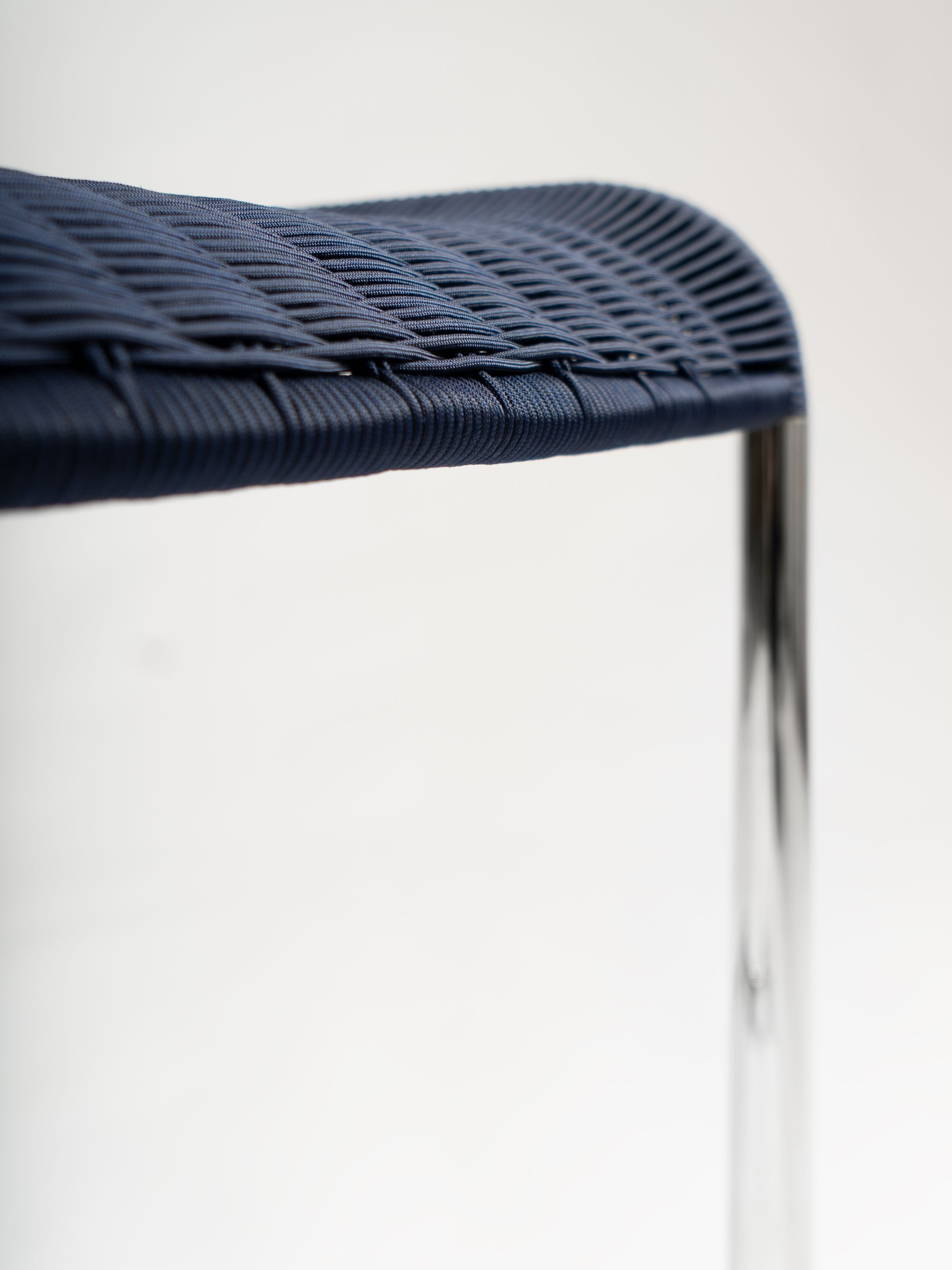 Detailaufnahme: Dunkelblauer B25 Kragstuhl von Tecta mit geflochtener Sitzfläche und verchromtem Stahlrohrgestell.