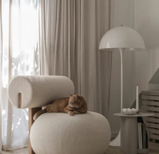 Beiger Sessel mit Bouclé-Bezug und Katze, Stehlampe im Hintergrund. Moderner Sessel für Wohnzimmer und Schlafzimmer.