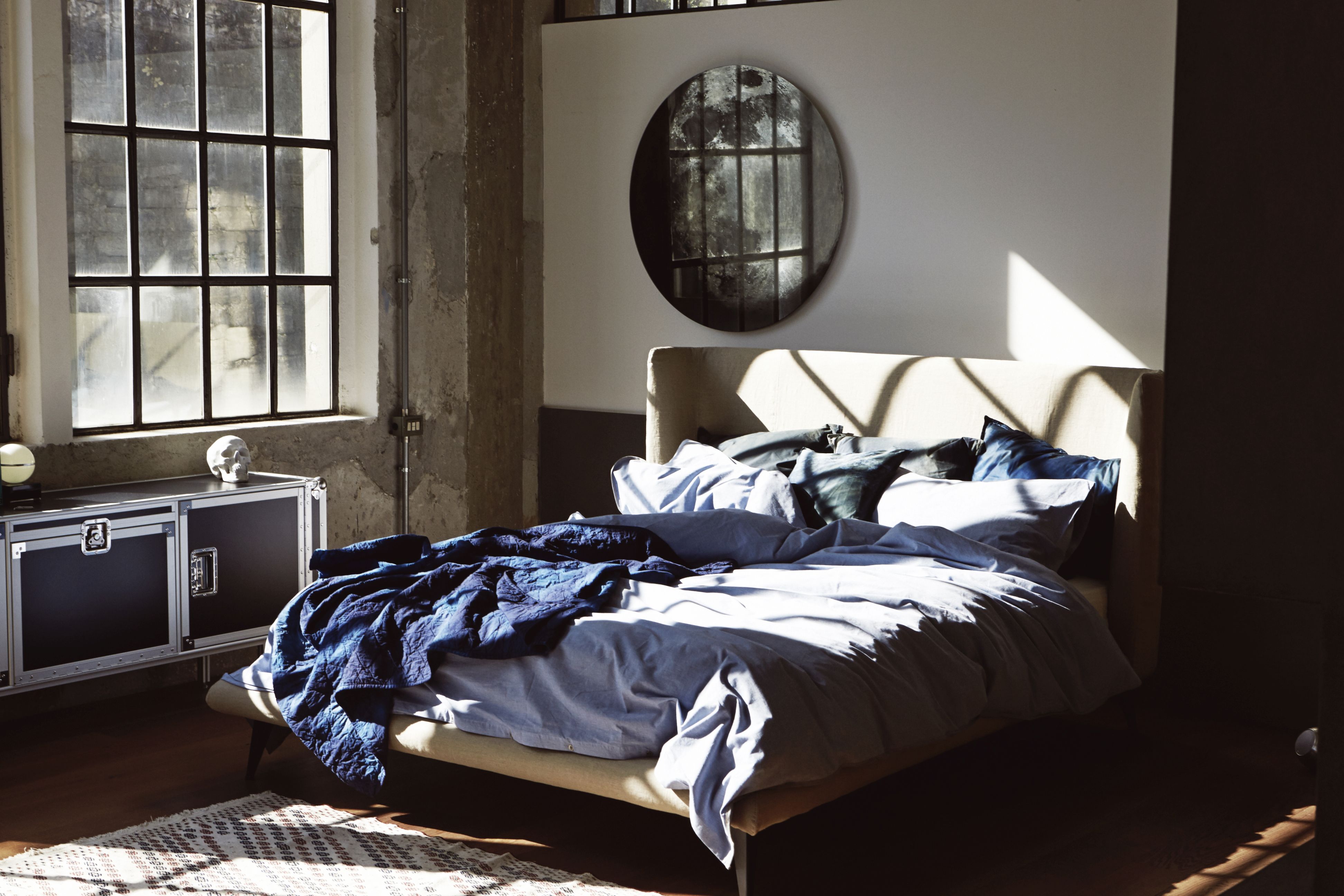 Schlafzimmer Interieur mit Total Sideboard von Moroso Diesel in Schwarz, Bett mit blauer Bettwäsche und rundem Spiegel.