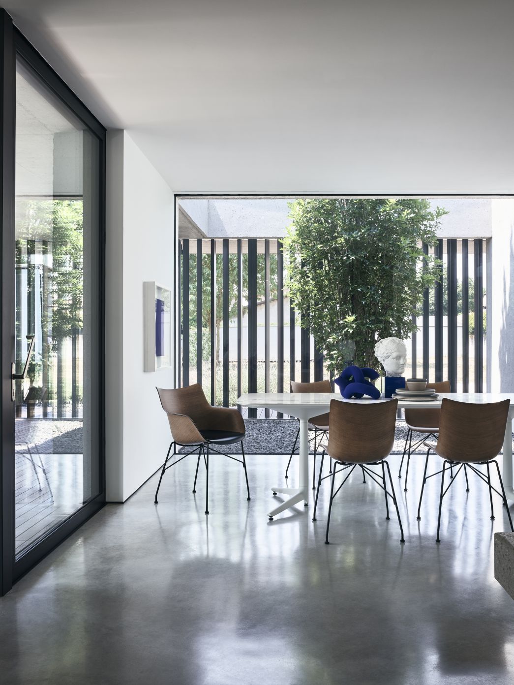 Esszimmer mit Kartell Q/WOOD Stühlen aus Holz und schwarzem Metallgestell an weißem Tisch.