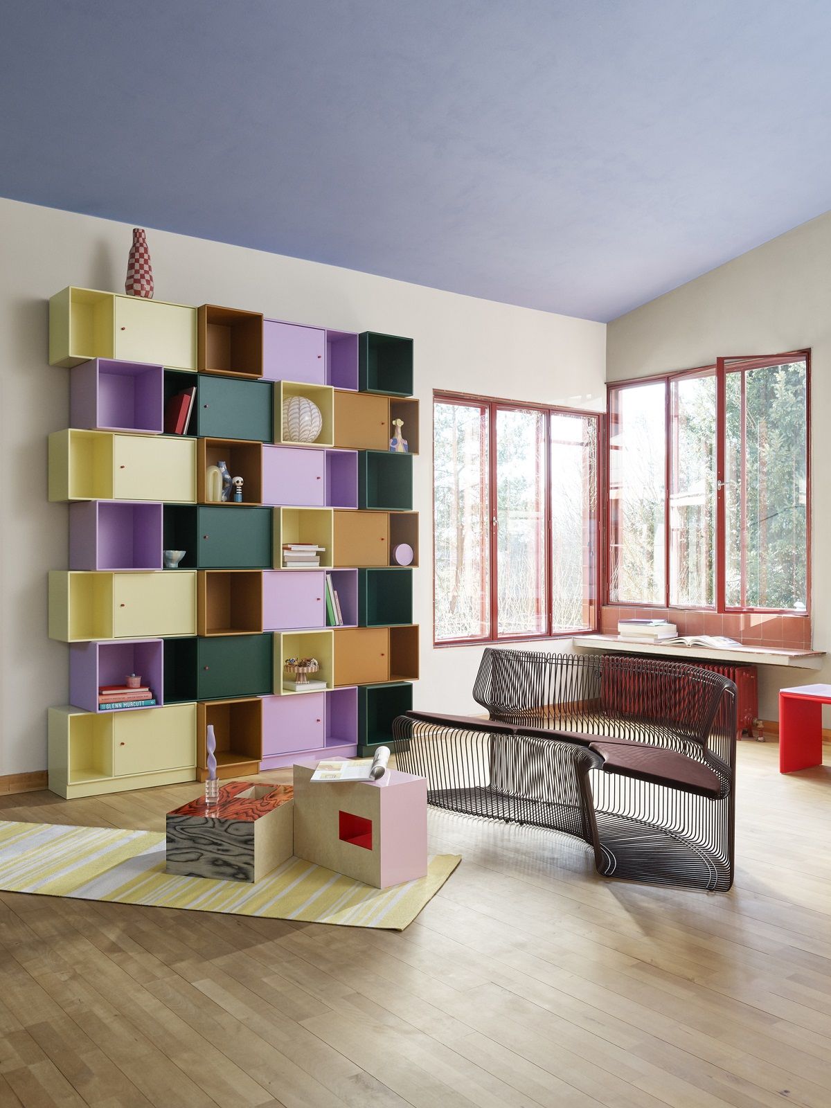 Wohnzimmer mit Montana Regalsystem in Pastellfarben und Pantonova Drahtstuhl als Sitzmodul.