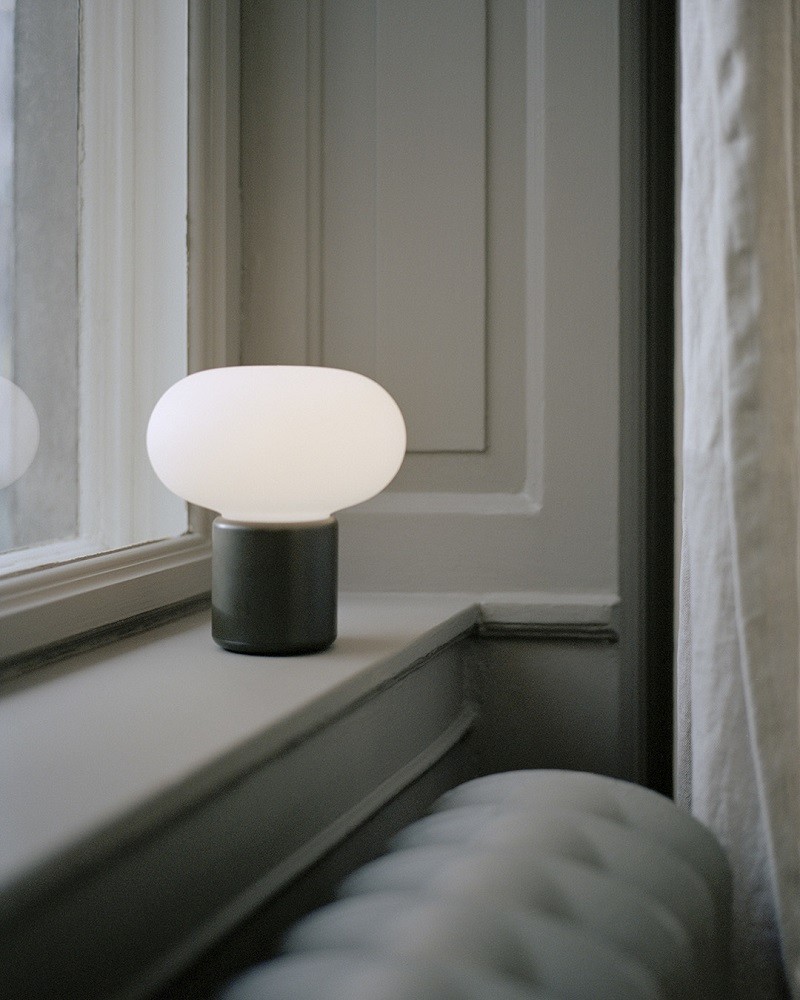 Karl-Johan Tischleuchte von New Works in Ochre Gelb auf einer Fensterbank. Akkuleuchte.