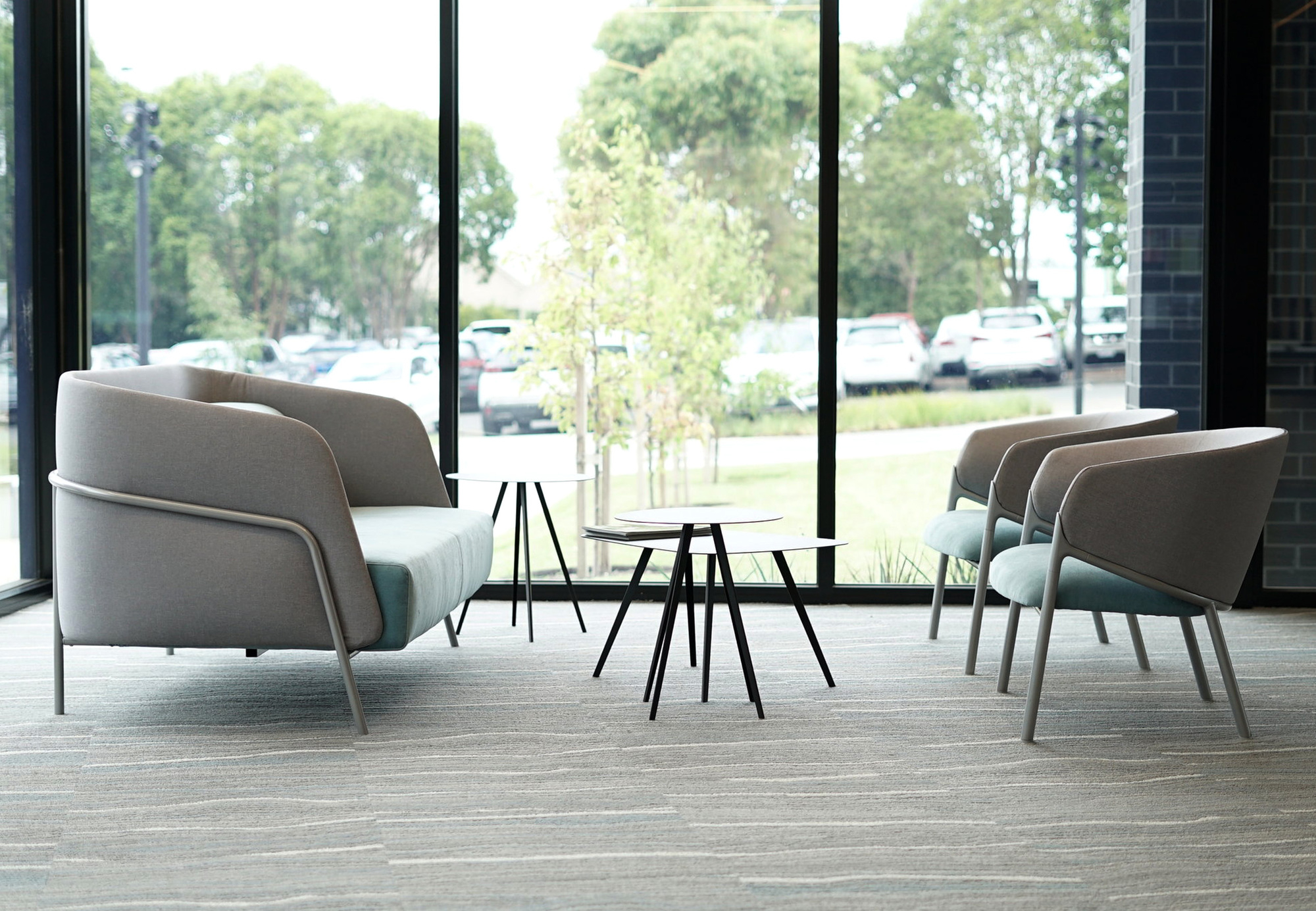 Innenaufnahme mit Agorà Beistelltischen und Sitzmöbeln vor einem Fenster. Design Beistelltisch mit schwarzem Gestell.