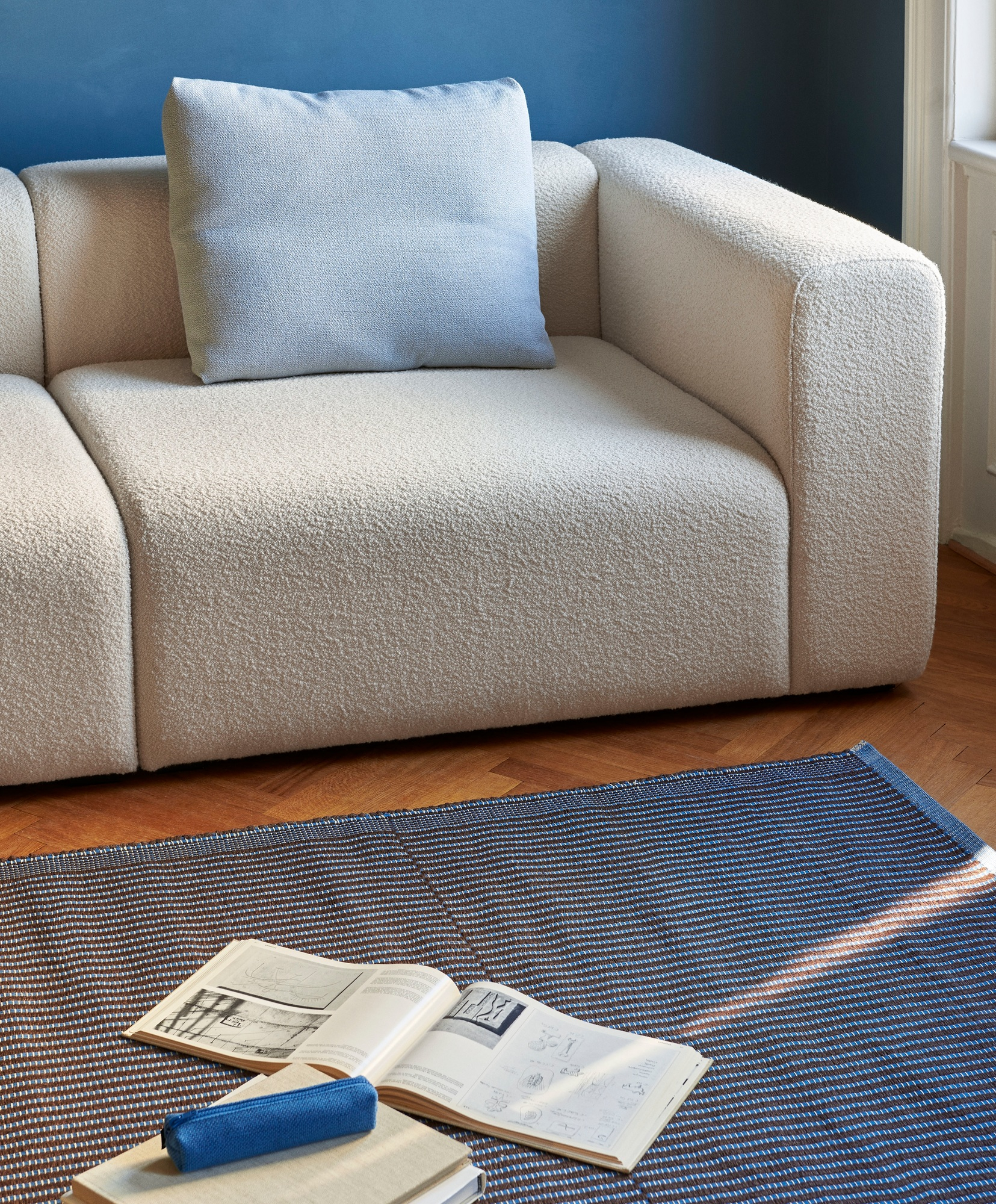 Detailaufnahme des Hay Tapis Teppichs in Blau-Braun, kombiniert mit einem beigen Sofa und Wohnaccessoires.