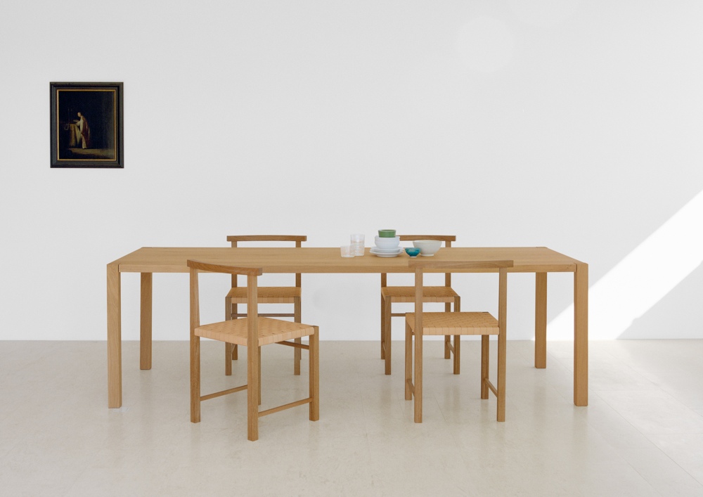 TA19 Sloane Tisch von e15 aus Eiche mit Stühlen und Geschirr vor weißer Wand.