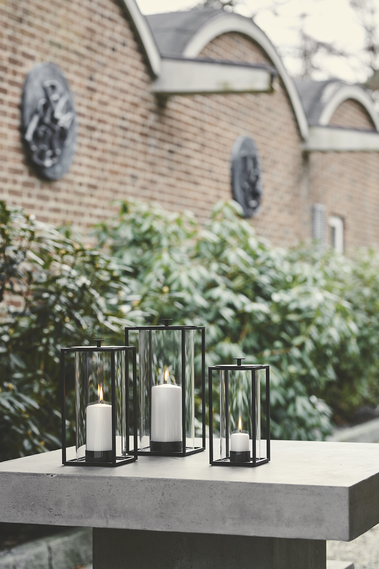 Drei moderne Windlichter aus Glas und schwarzem Metall mit brennenden Kerzen für Garten und Terrasse.