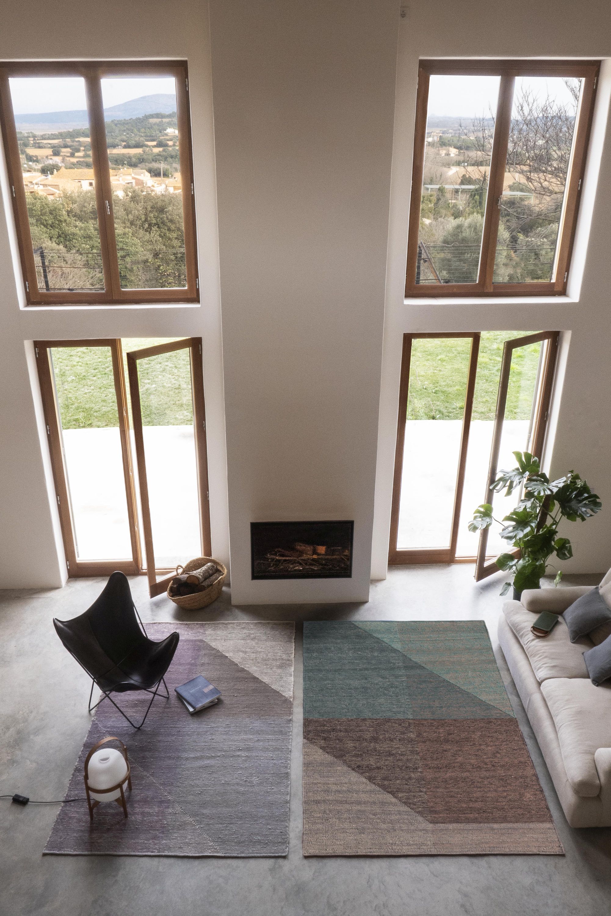 Zwei Nanimarquina Capas Teppiche 170x240 cm im modernen Wohnzimmer mit Sessel und Kamin. Designteppiche für stilvolles Wohnen.