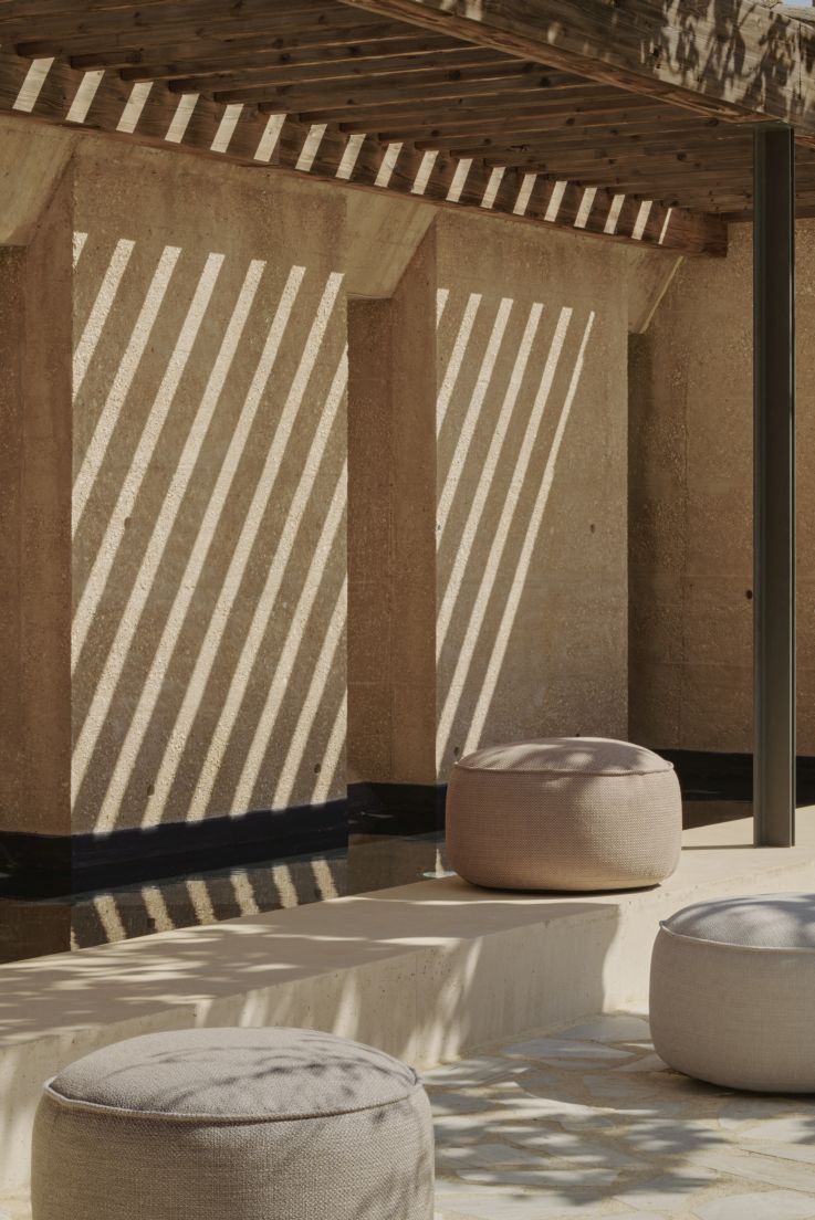 Drei graue Outdoor Sitzhocker im Donut-Design von Ethnicraft vor einer Wand mit Schattenmuster.