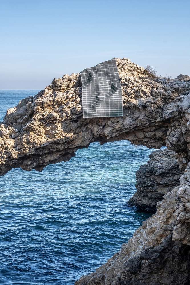 Nanimarquina Tiles Teppich #3 auf Felsen mit Meer im Hintergrund, moderner grau-weißer Designer Teppich.