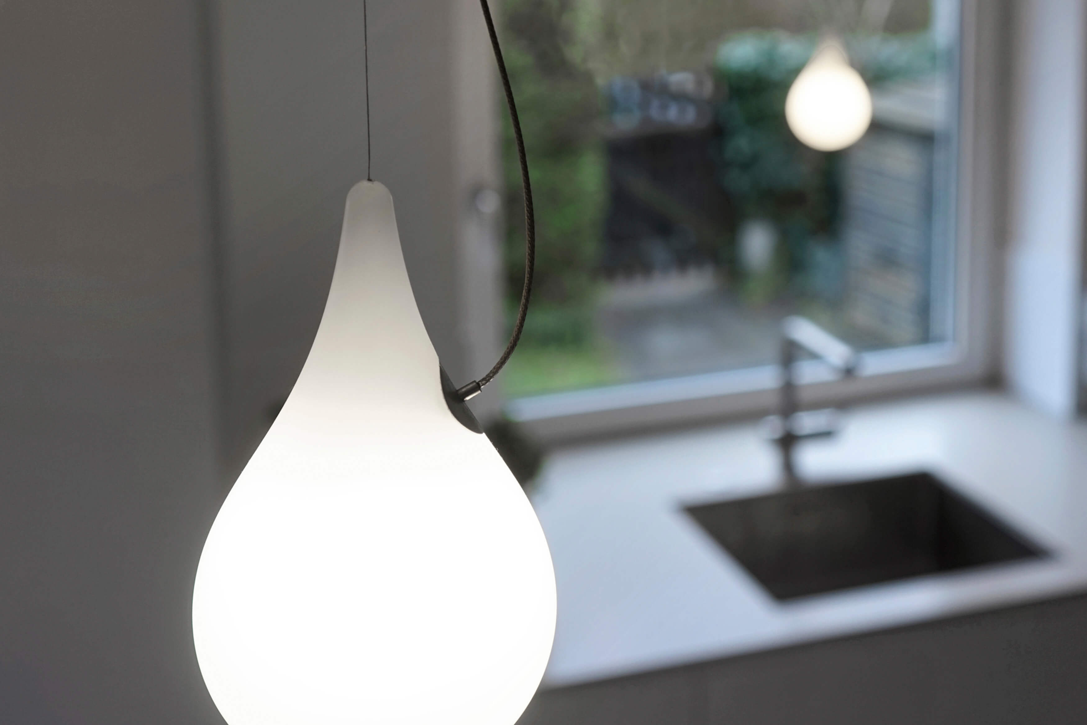 Nahaufnahme der Liquid Light Pendelleuchte von Next, Tropfenform, modernes Design, warmes Licht.