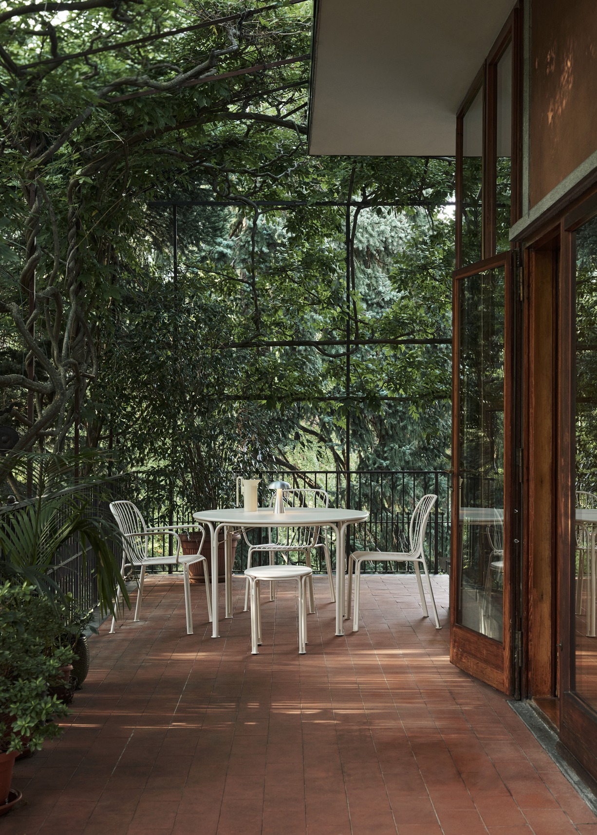 AndTradition Thorvald Stuhl SC94 für den Außenbereich auf einer Terrasse mit Tisch und Pflanzen.