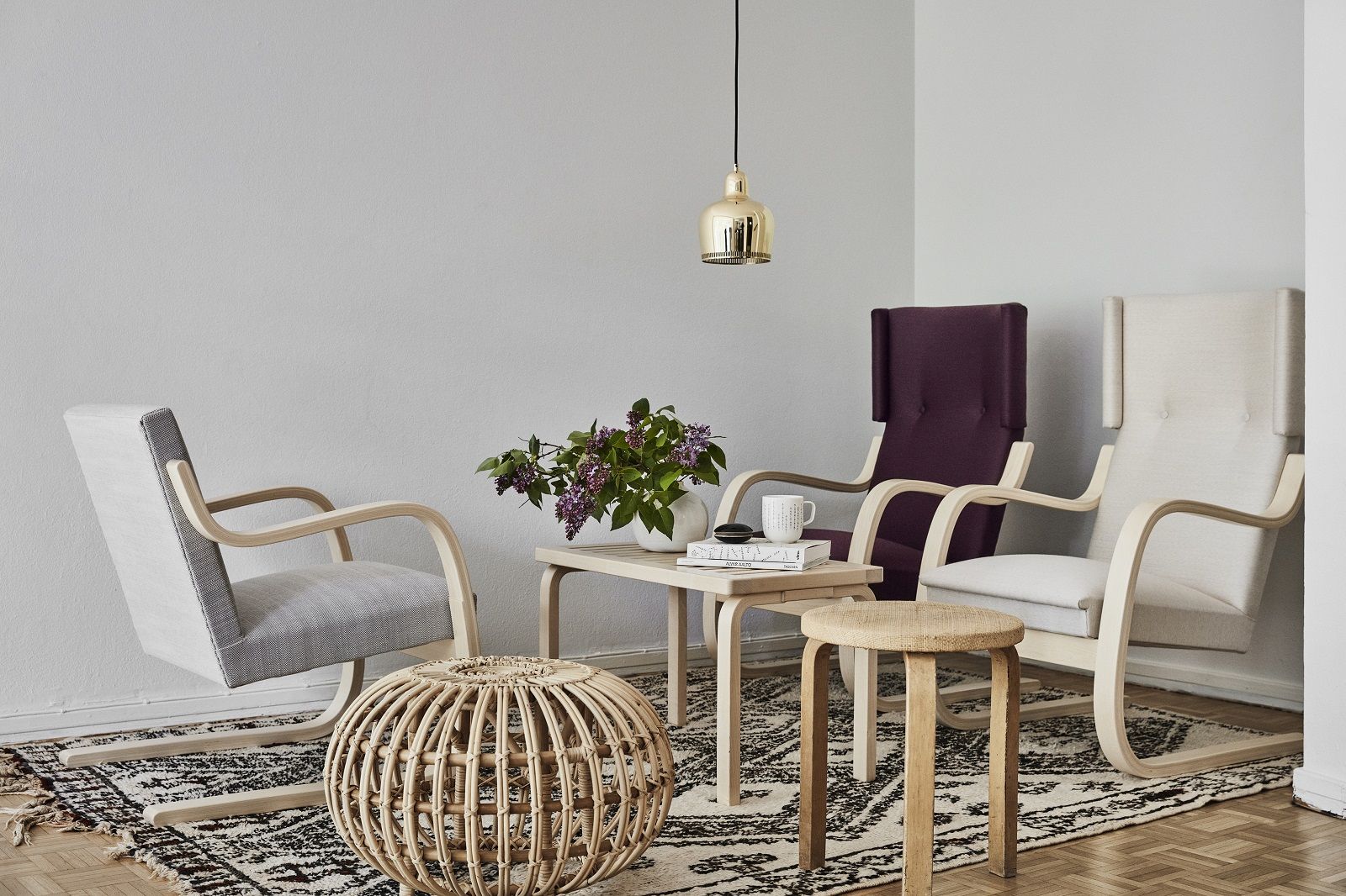 Wohnzimmer-Szene mit Artek Bank, Sesseln, Tisch und Hocker auf einem gemusterten Teppich.