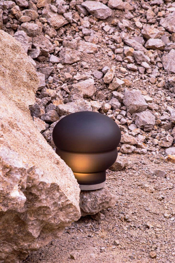 Kumo Tischleuchte von Pulpo, kleine, moderne Lampe in Weiß, auf Steinen platziert.