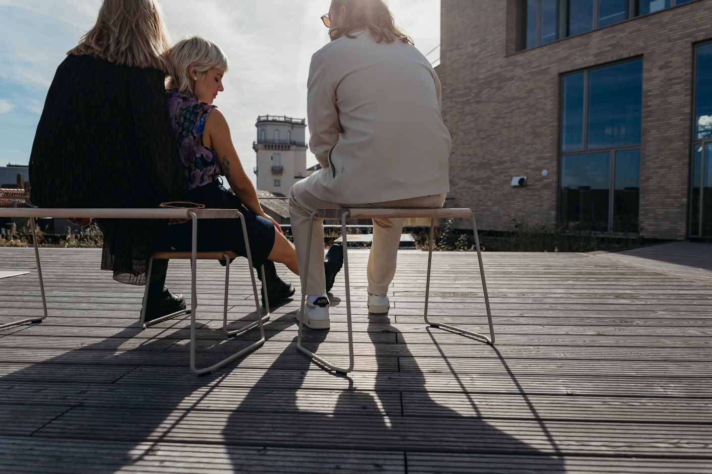 Drei Personen sitzen auf weißen D:003 Beistellhockern von Fuchs & Habicht im Freien.