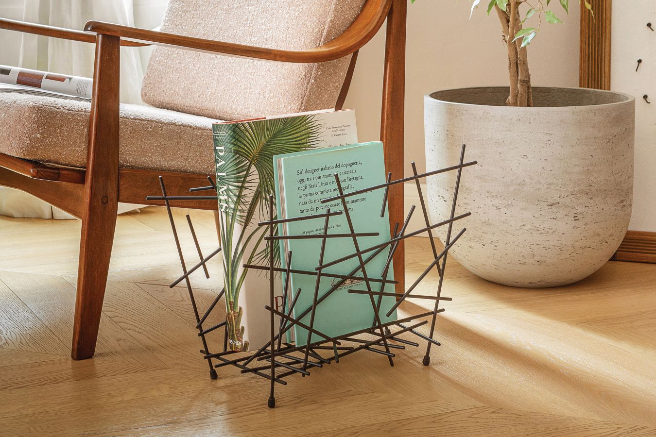 Schwarzer Alessi Zeitschriftenhalter "Blow Up" neben Sessel und Zimmerpflanze, moderne Wohnaccessoires und Designobjekte.