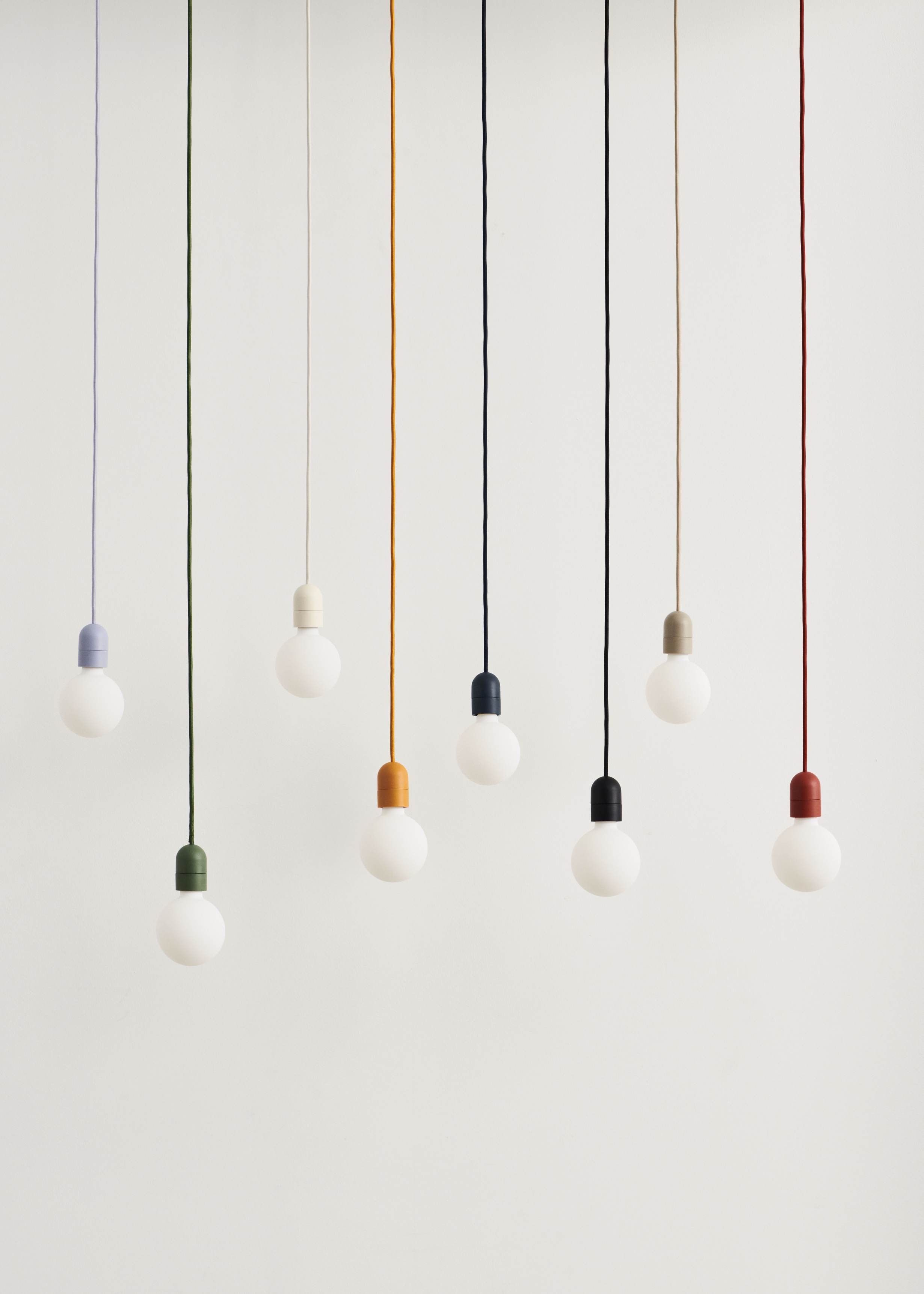 Mehrere Hay Pendelleuchten mit farbigen Textilkabeln und Fassungen, darunter rostrot, für moderne Innenbeleuchtung.