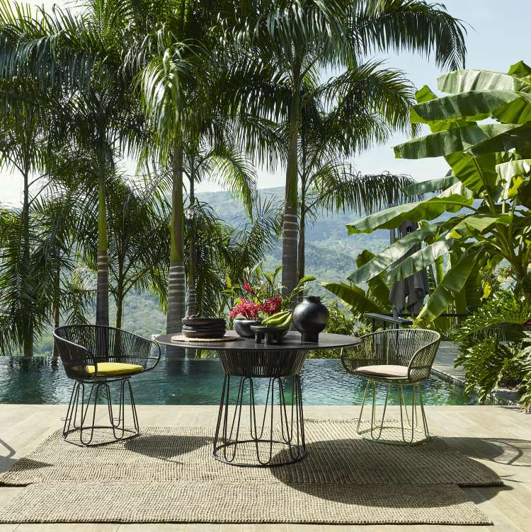 Ames Circo Dining Chair Outdoor mit gelbem Sitzkissen und Tisch im tropischen Garten.