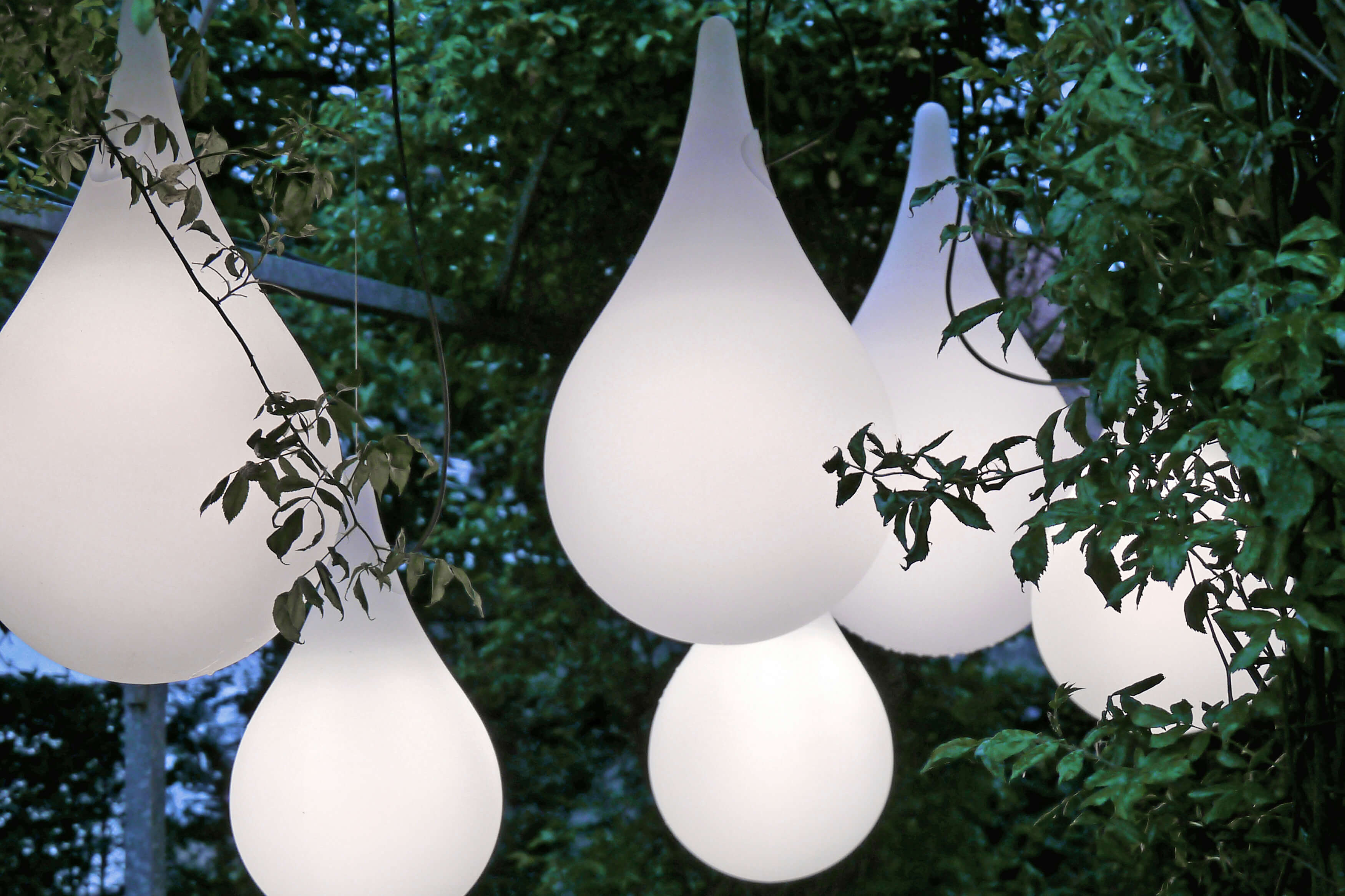 Mehrere Liquid Light Drop Pendelleuchten von Next im Außenbereich, umgeben von Grün.