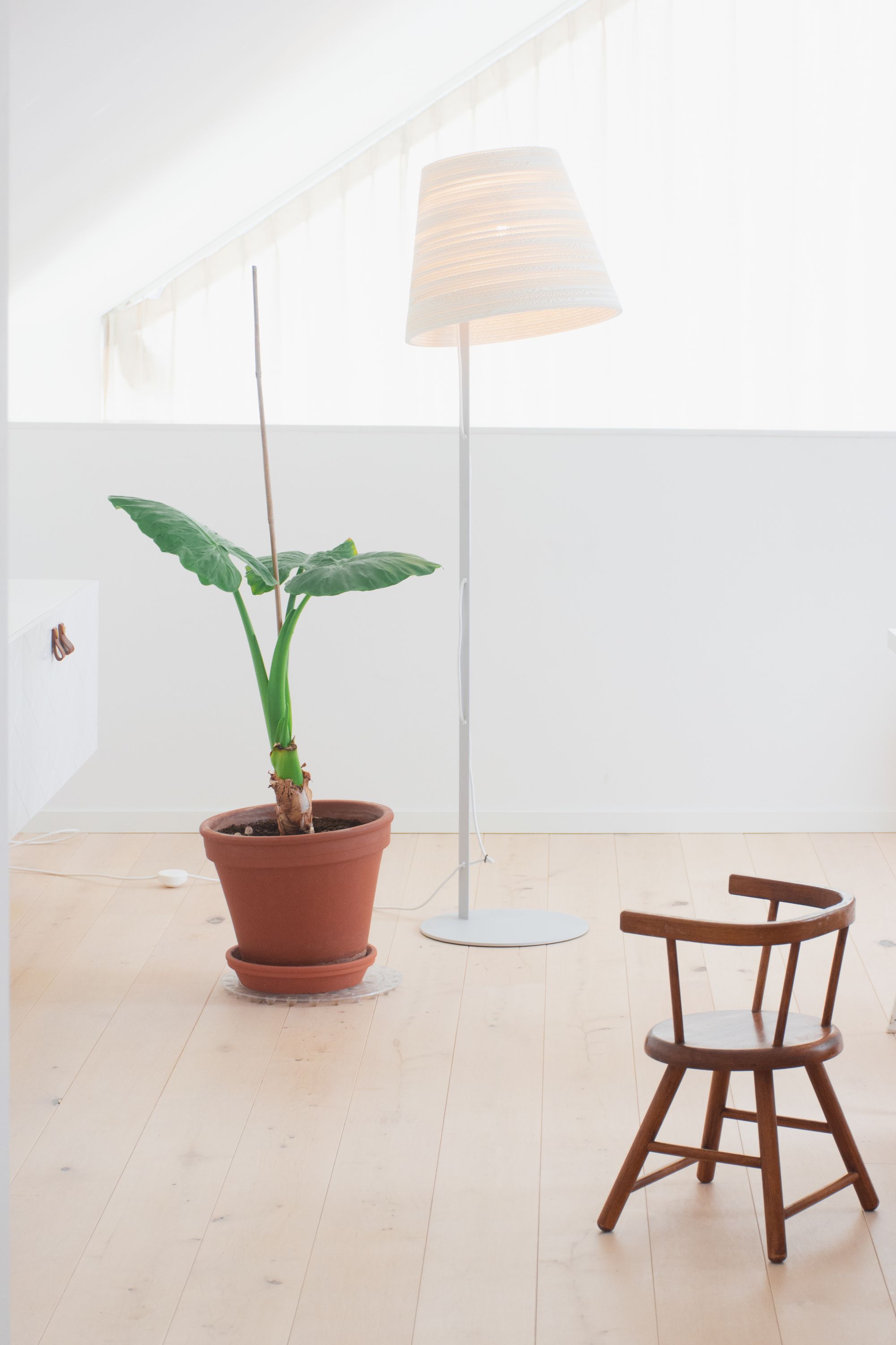 Helle Tilt Stehleuchte Scraplights von Graypants im minimalistischen Raum, neben Zimmerpflanze und Holzstuhl.