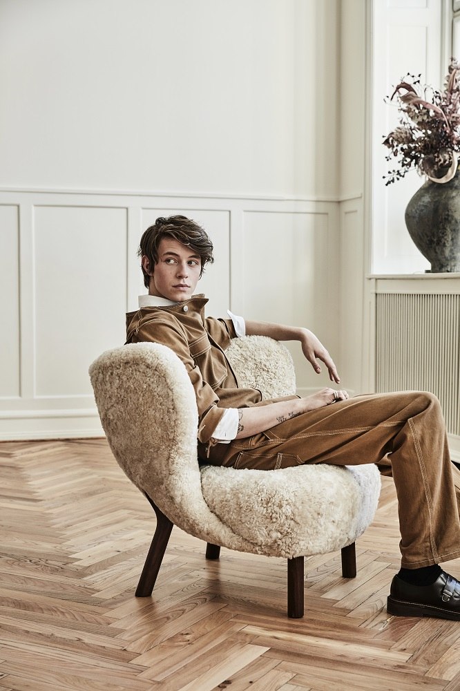 Mann sitzt im Little Petra Sessel von &Tradition. Der Lounge Sessel ist aus Walnuss und Moonlight-Wolle.