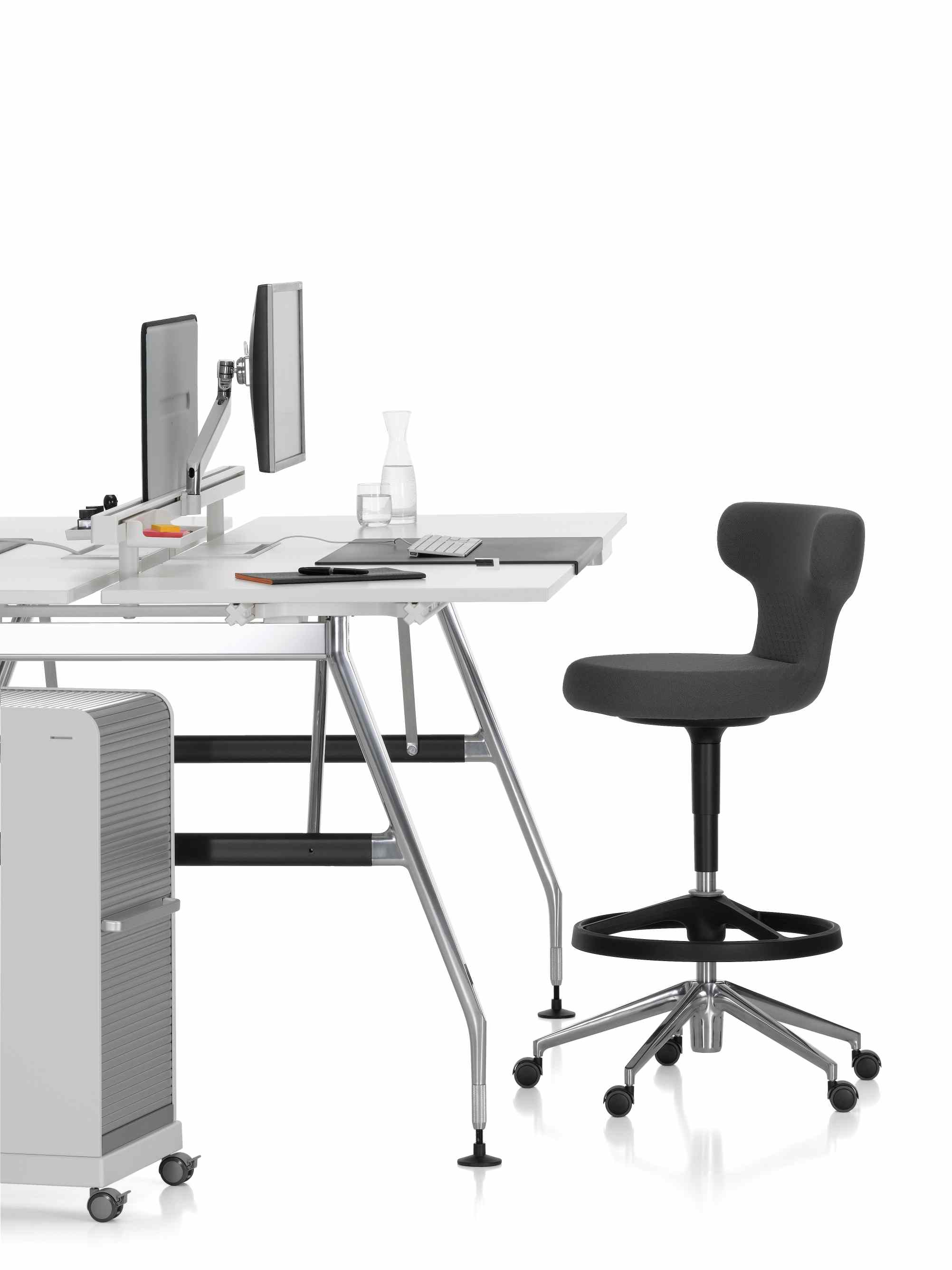 Büroarbeitsplatz mit Vitra Rollcontainer, Schreibtisch, Bürostuhl und Monitoren vor weißem Hintergrund.