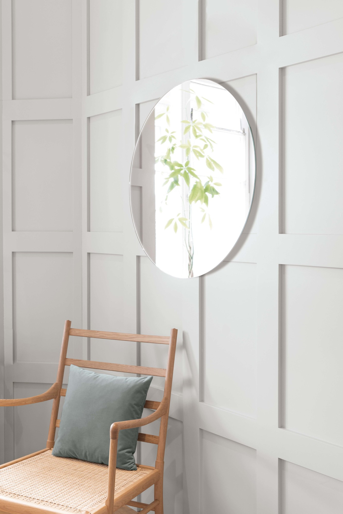 Runder Schönbuch Spiegel, Durchmesser 75 cm, an weißer Wand über einem Holzstuhl.