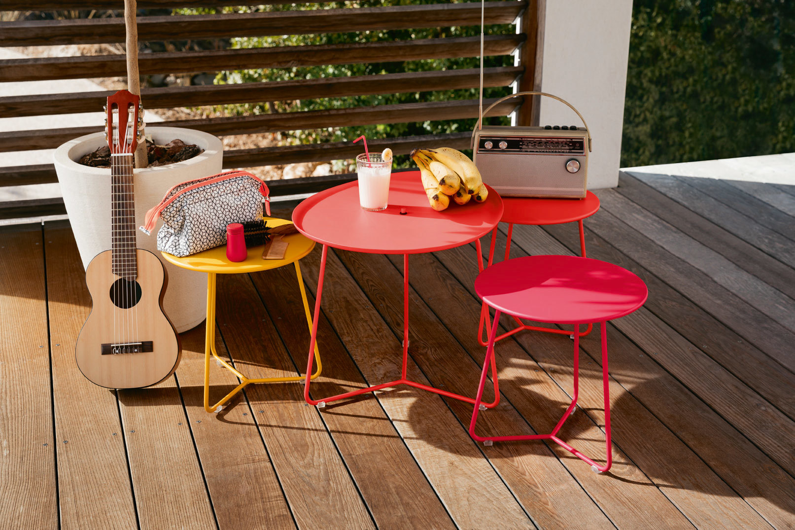 Kleiner, runder Outdoor Tisch von Fermob in verschiedenen Farben auf einer Holzterrasse.