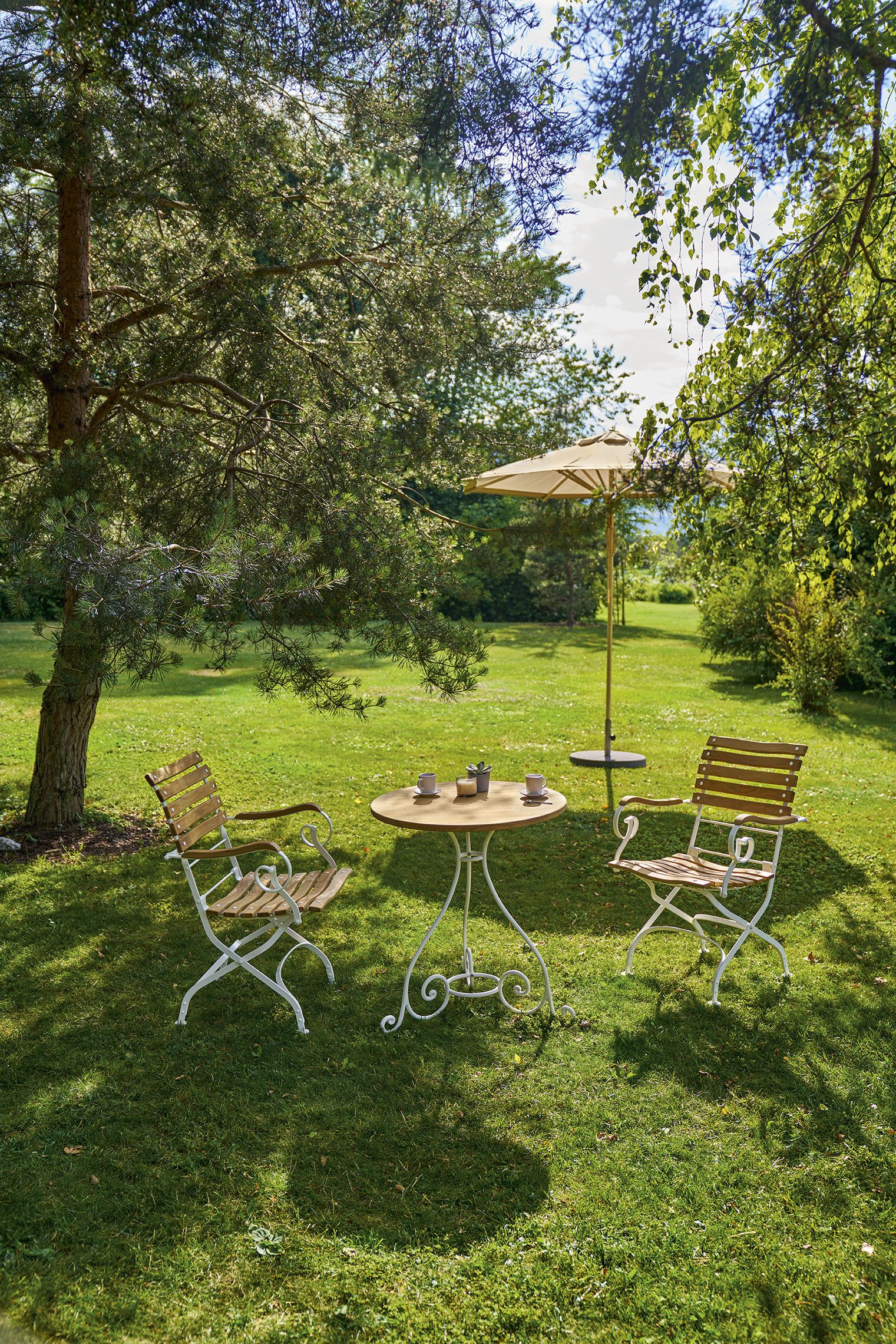 Weishäupl Teakschirm und Gartenmöbel-Set auf Rasenfläche, bestehend aus zwei Stühlen, Tisch und Sonnenschirm.