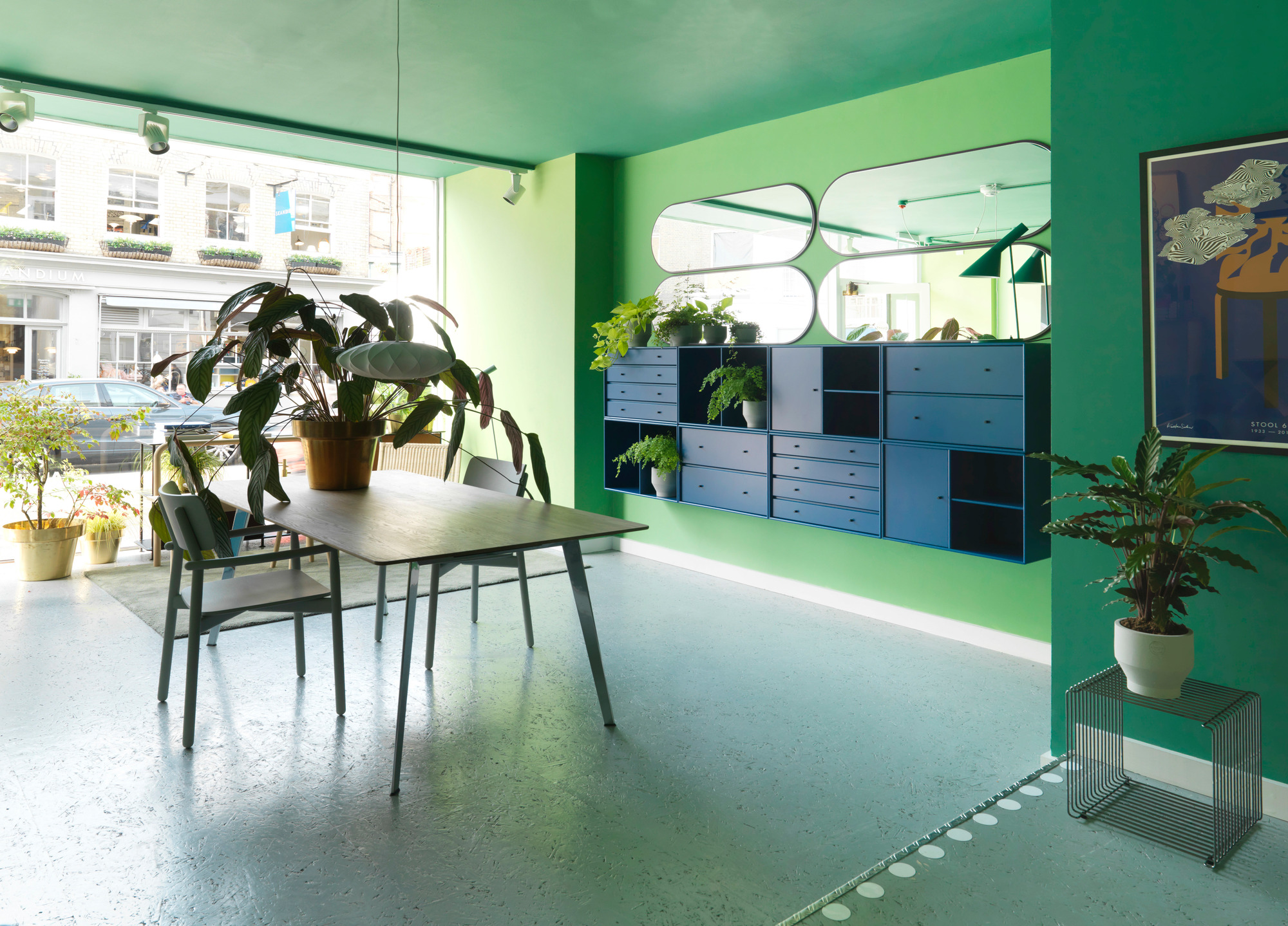 Innenaufnahme mit Panton Wire Cube Beistelltisch, Couchtisch und Montana Regalsystem in einem grün gestrichenen Raum.