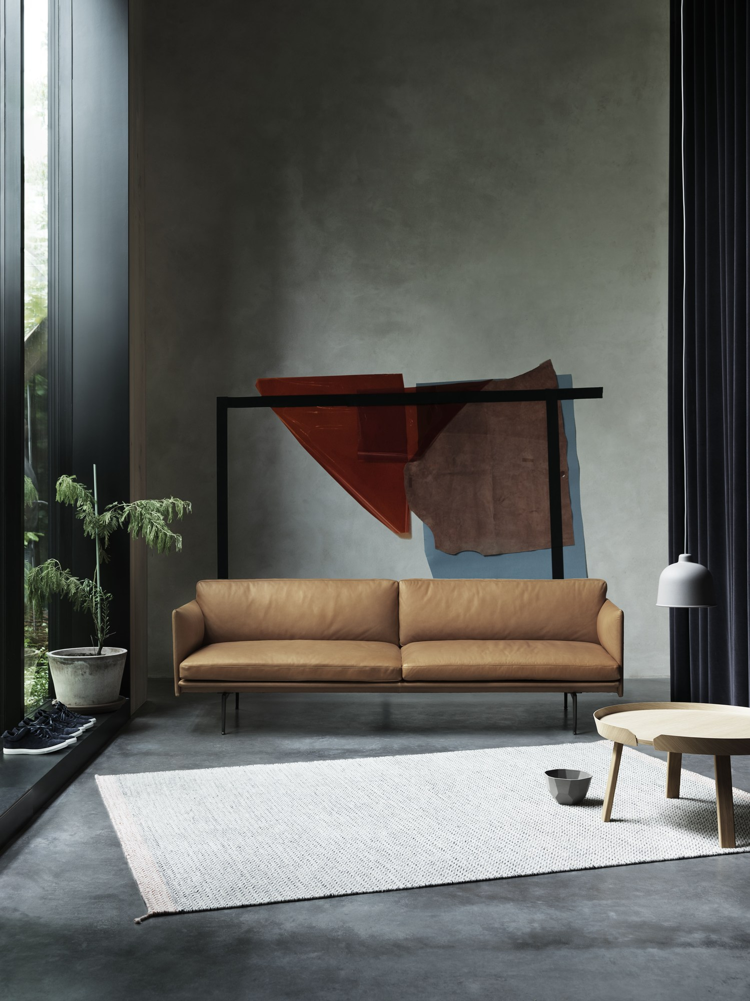 Helles Wohnzimmer mit braunem Muuto Outline Sofa, Teppich und Kunstwerk an der Wand.