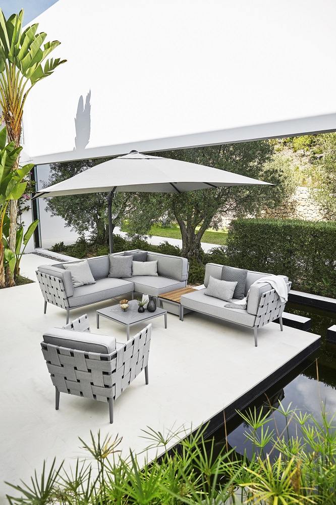 Weißer Hyde Luxe Sonnenschirm von Cane-Line mit Fuß über einer modernen Lounge-Garnitur im Garten.