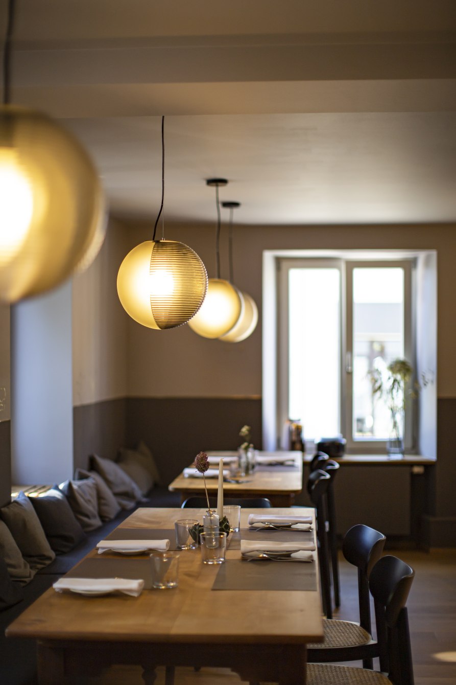 Reihe von Stellar Pendelleuchten von Pulpo über gedeckten Holztischen in einem Restaurant.