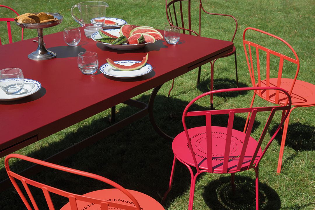 Roter Louvre Stuhl von Fermob mit passendem Gartentisch und Melonen auf dem Rasen.