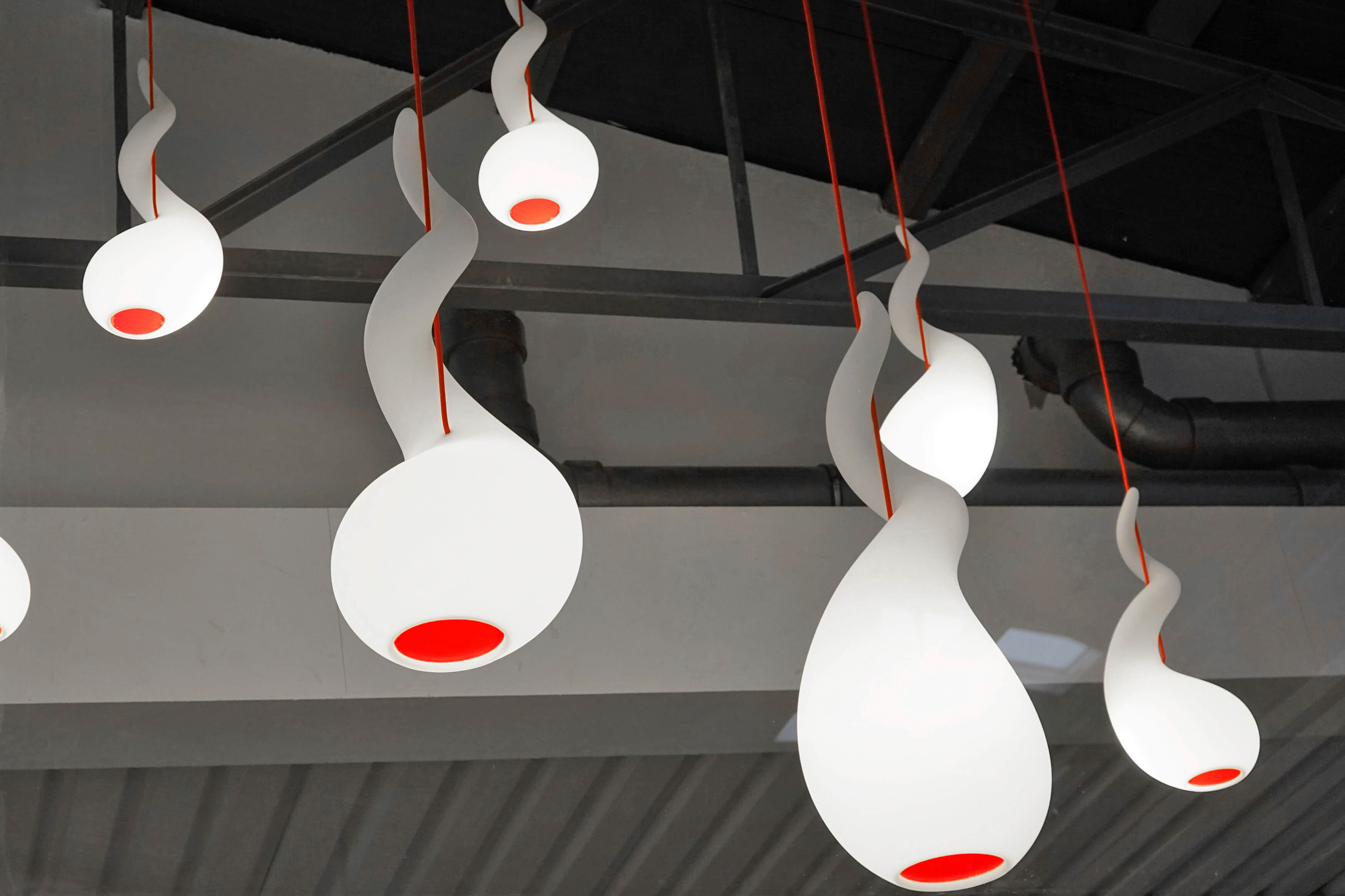 Alien PL Pendelleuchte Next: Mehrere moderne, weiße Pendelleuchten mit rotem Akzent an der Decke.