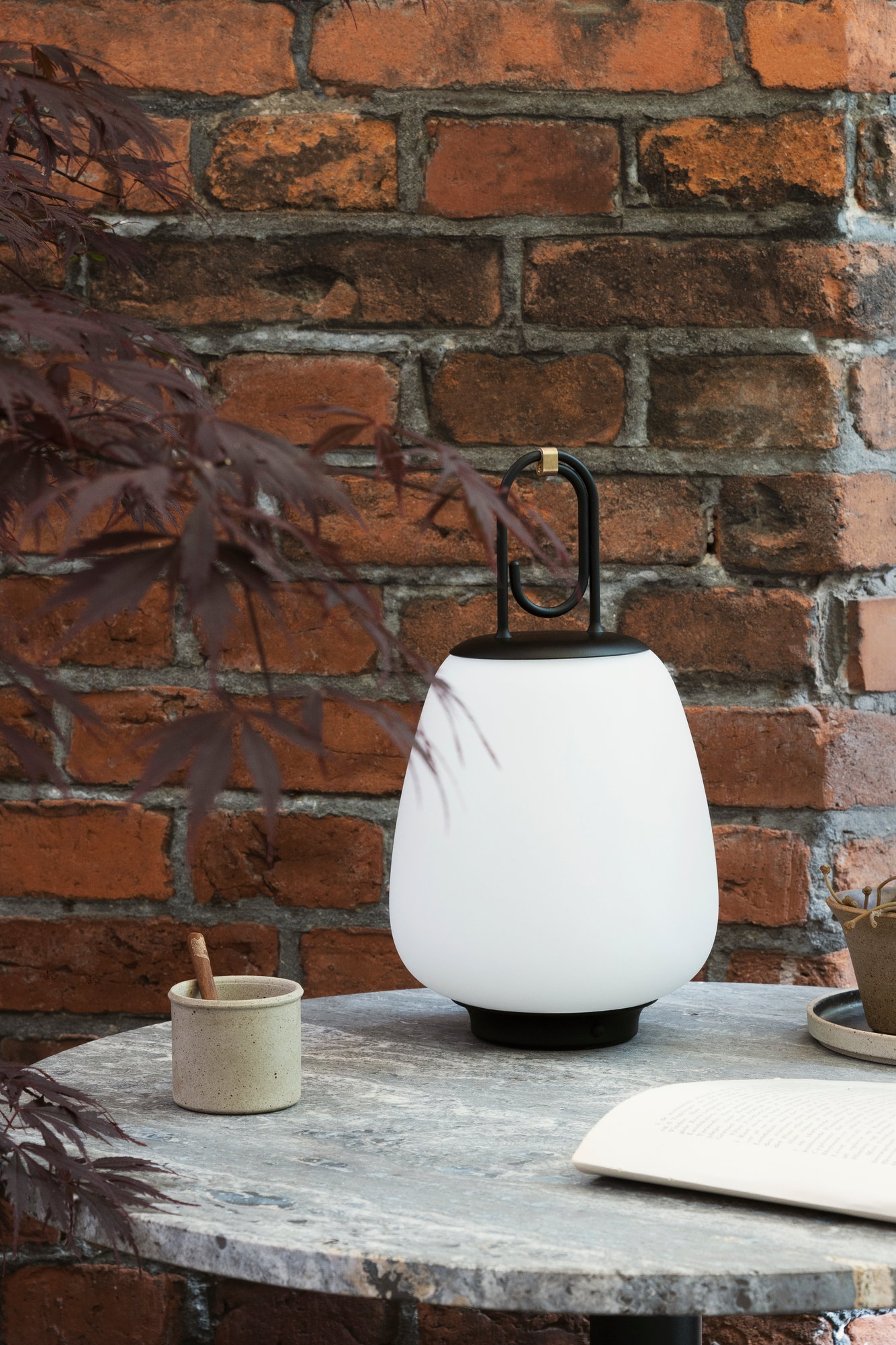 Lucca Akkuleuchte schwarz von AndTradition auf Tisch, stimmungsvolle Beleuchtung für drinnen und draußen.