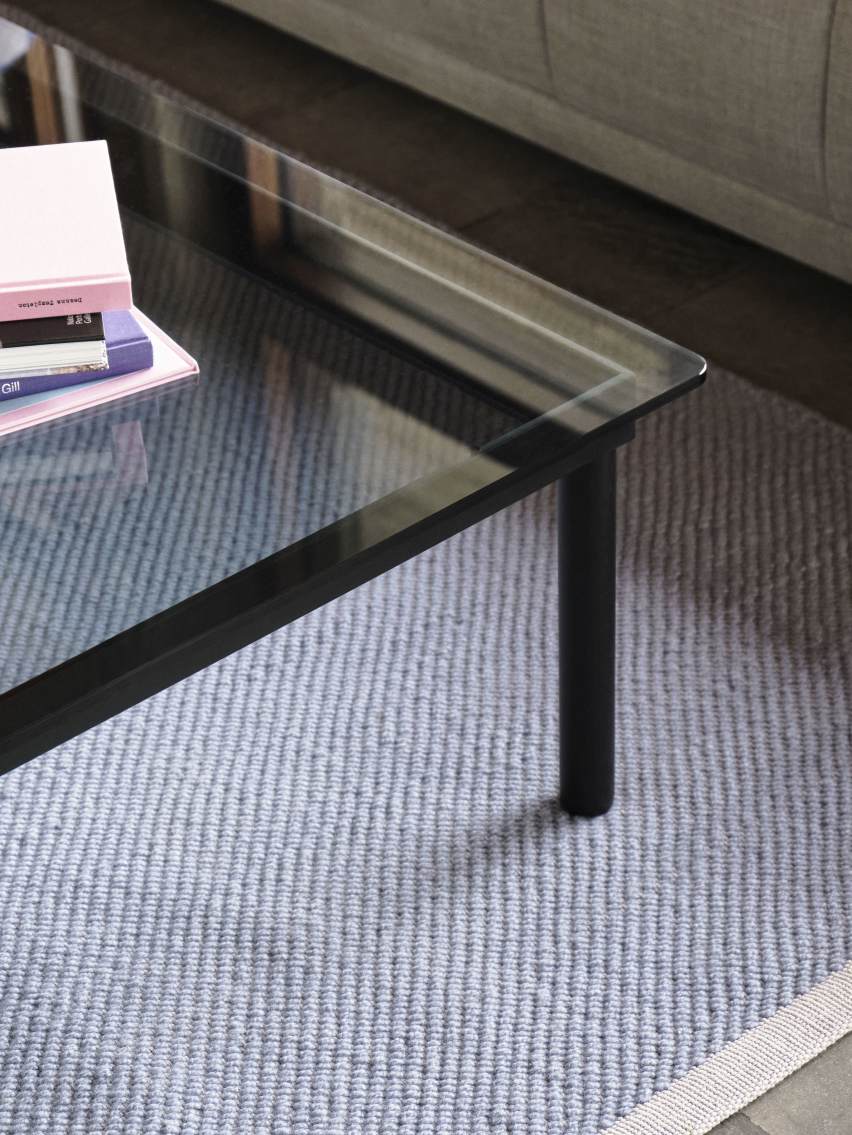 Detailaufnahme vom Kofi Couchtisch 100x100 cm von Hay mit Glasplatte und schwarzen Beinen auf Teppich.
